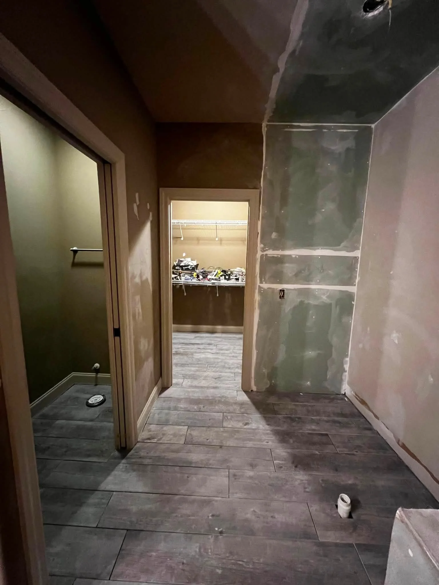 Bathroom undergoing renovation with partially installed tile walls, an open closet or storage area in the background with tools, and a wooden floor.