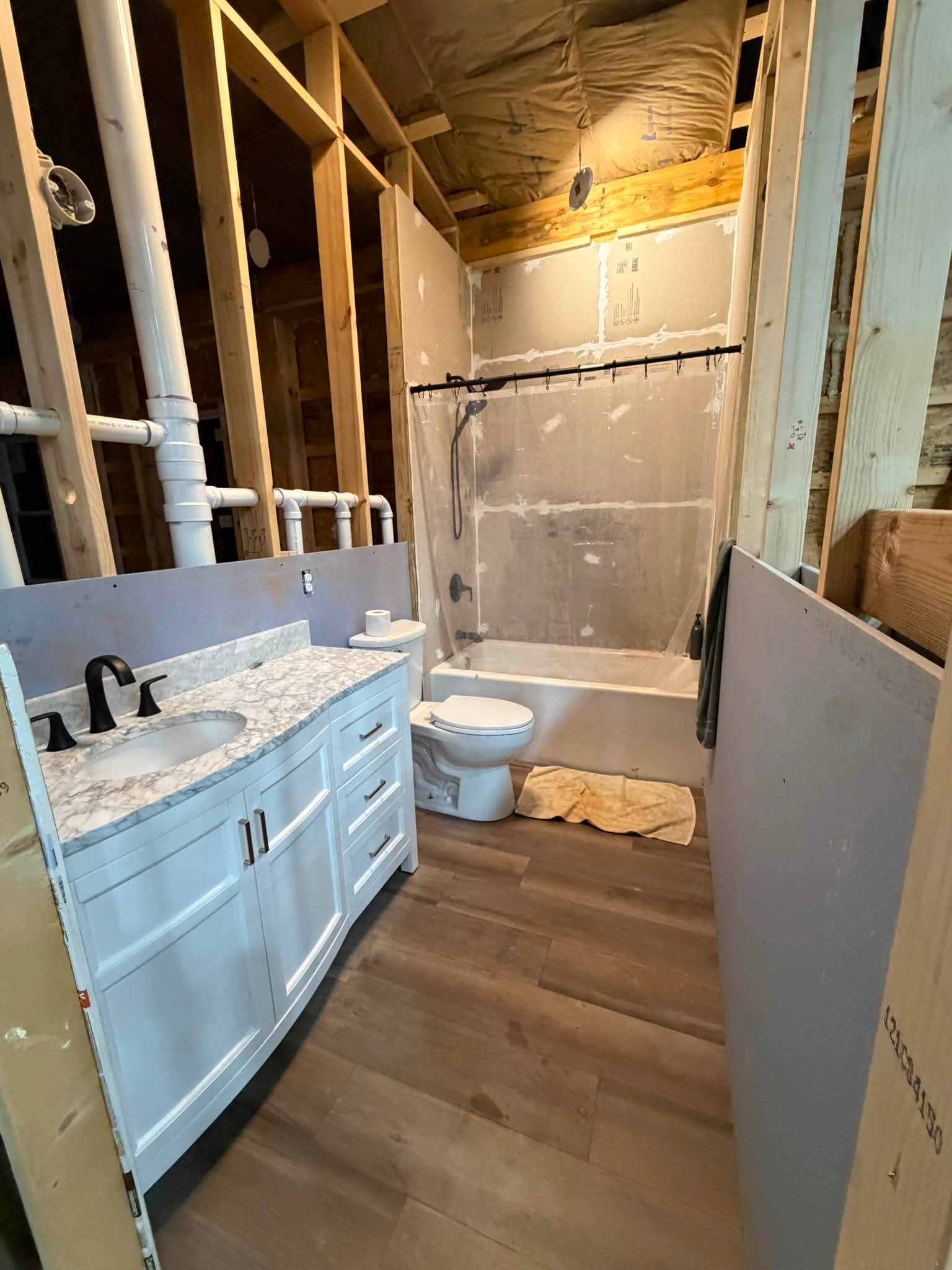 Bathroom under construction with a white vanity, a bathtub with a shower, plumbing pipes, and drywall in progress.