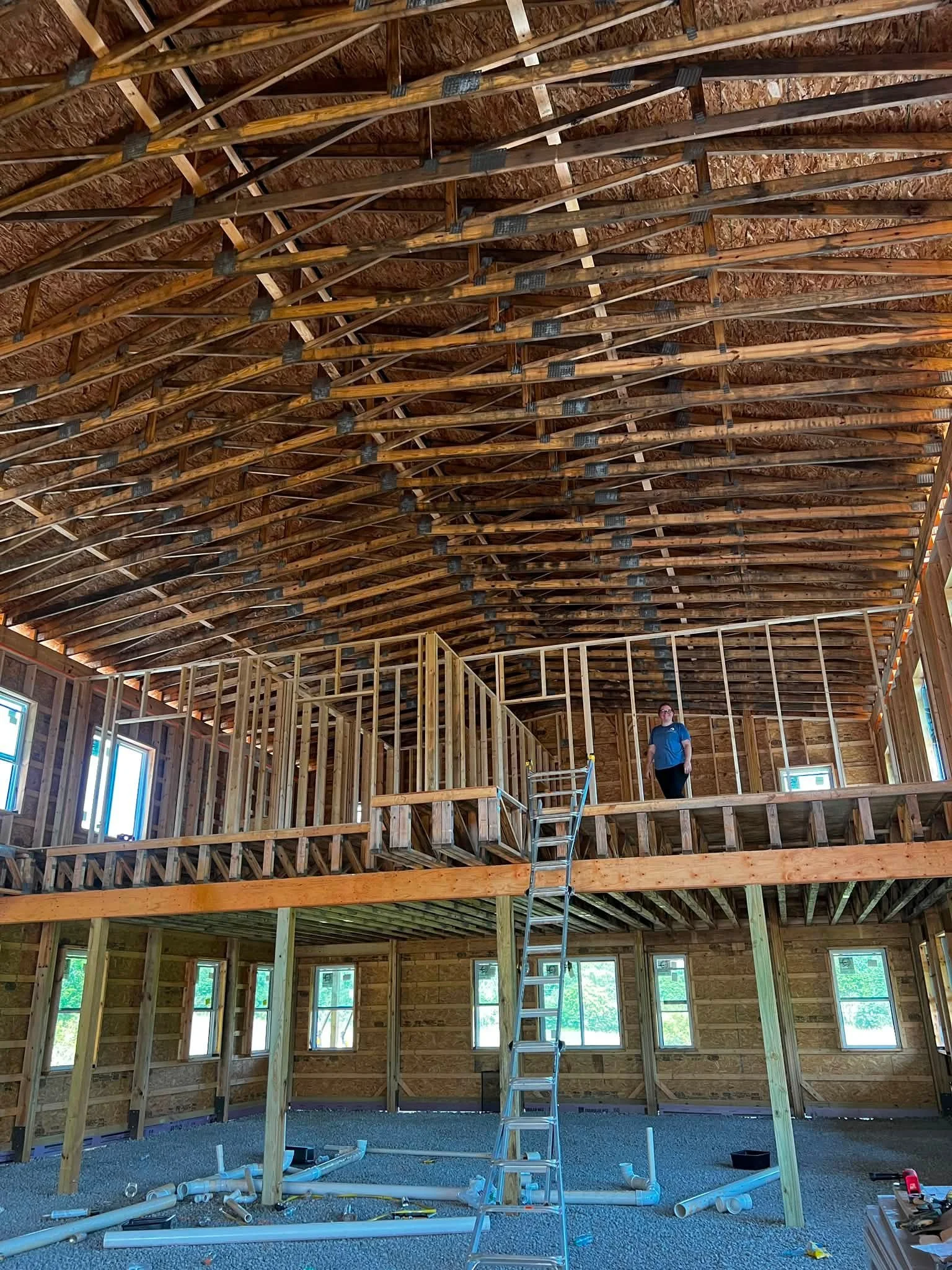 The interior of a house under construction with exposed wooden framing, a ladder, and construction tools.
