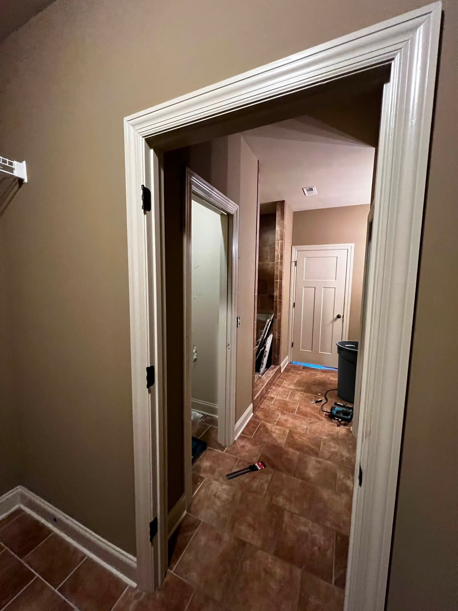 A hallway under renovation with doors removed, tools on the floor, and some construction materials visible.