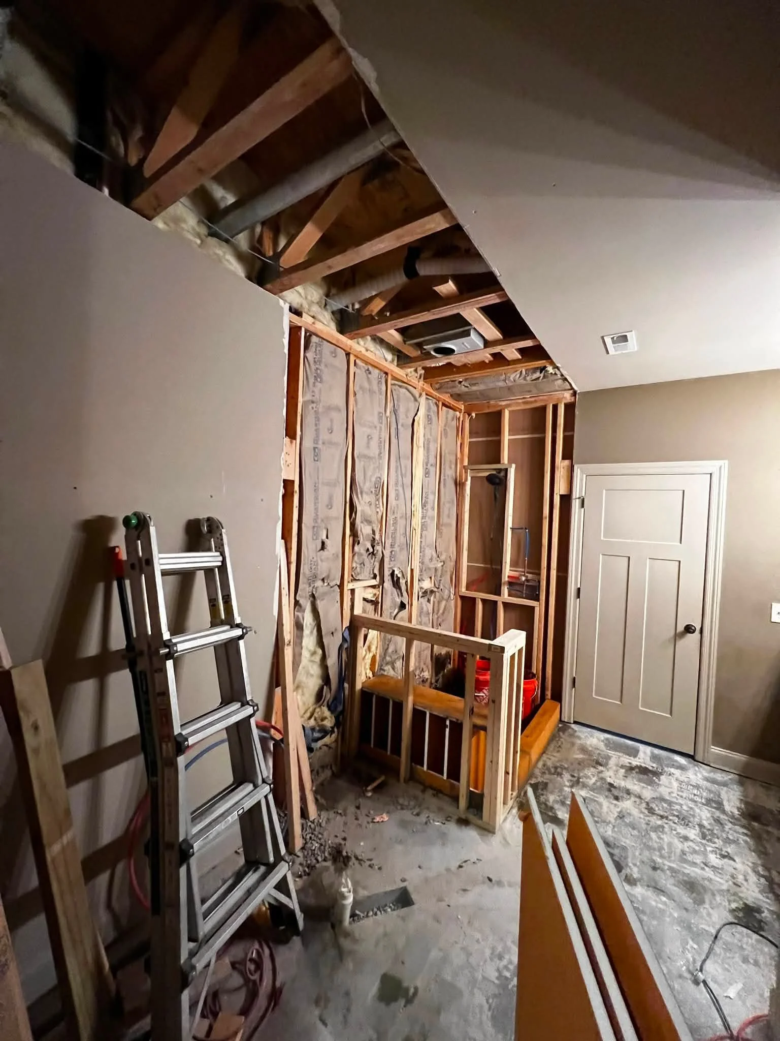 Room under construction with exposed wall framing, insulation, and a ladder leaning against the wall.