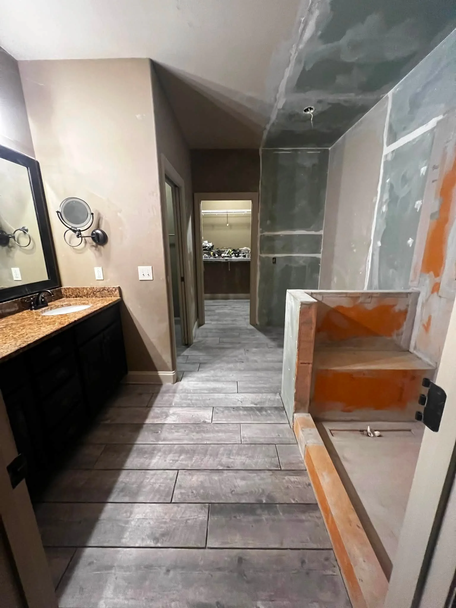 Bathroom undergoing renovation with unfinished cabinets, walls, and ceiling, with construction materials and tools visible.