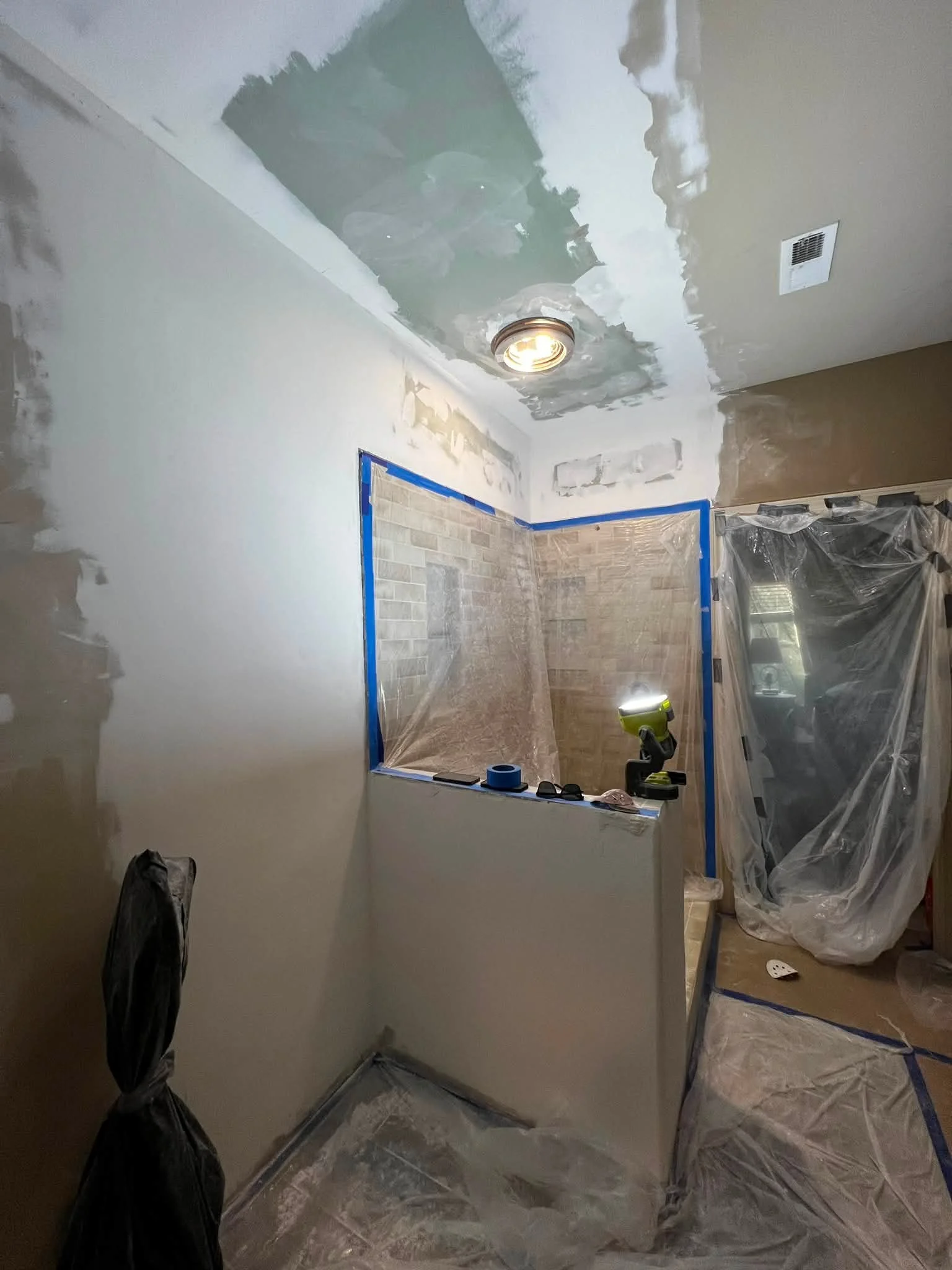 Interior of a room under renovation with painted walls, partially drywall ceiling, plastic coverings, and construction tools.