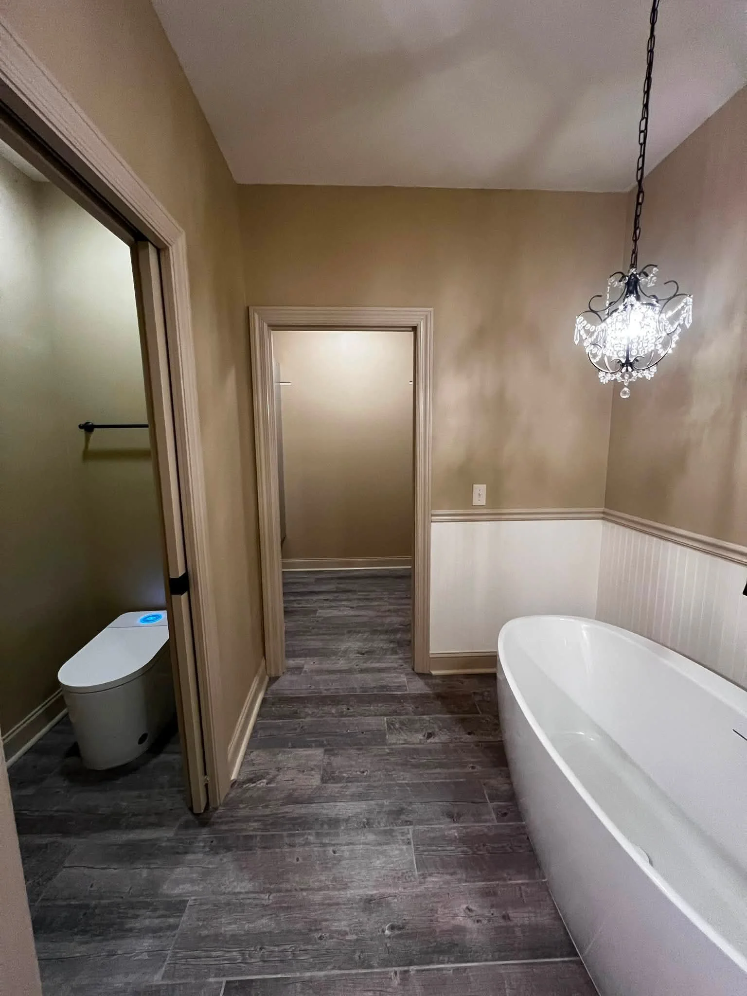 Bathroom with a freestanding bathtub, a chandelier light fixture, beige walls, and wood-look flooring.