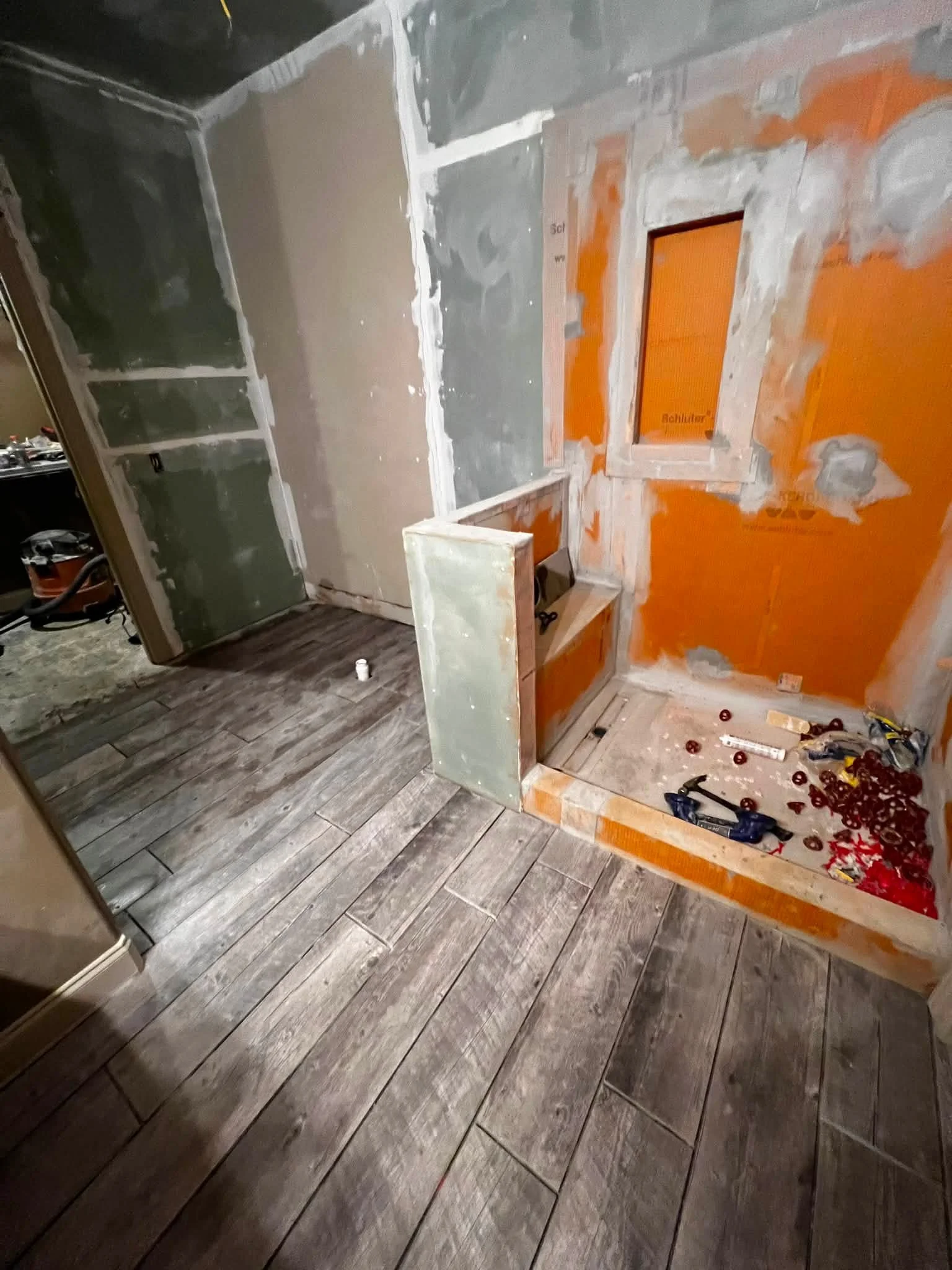 Room under renovation with partially installed flooring and walls in progress, tools and materials scattered on the floor.