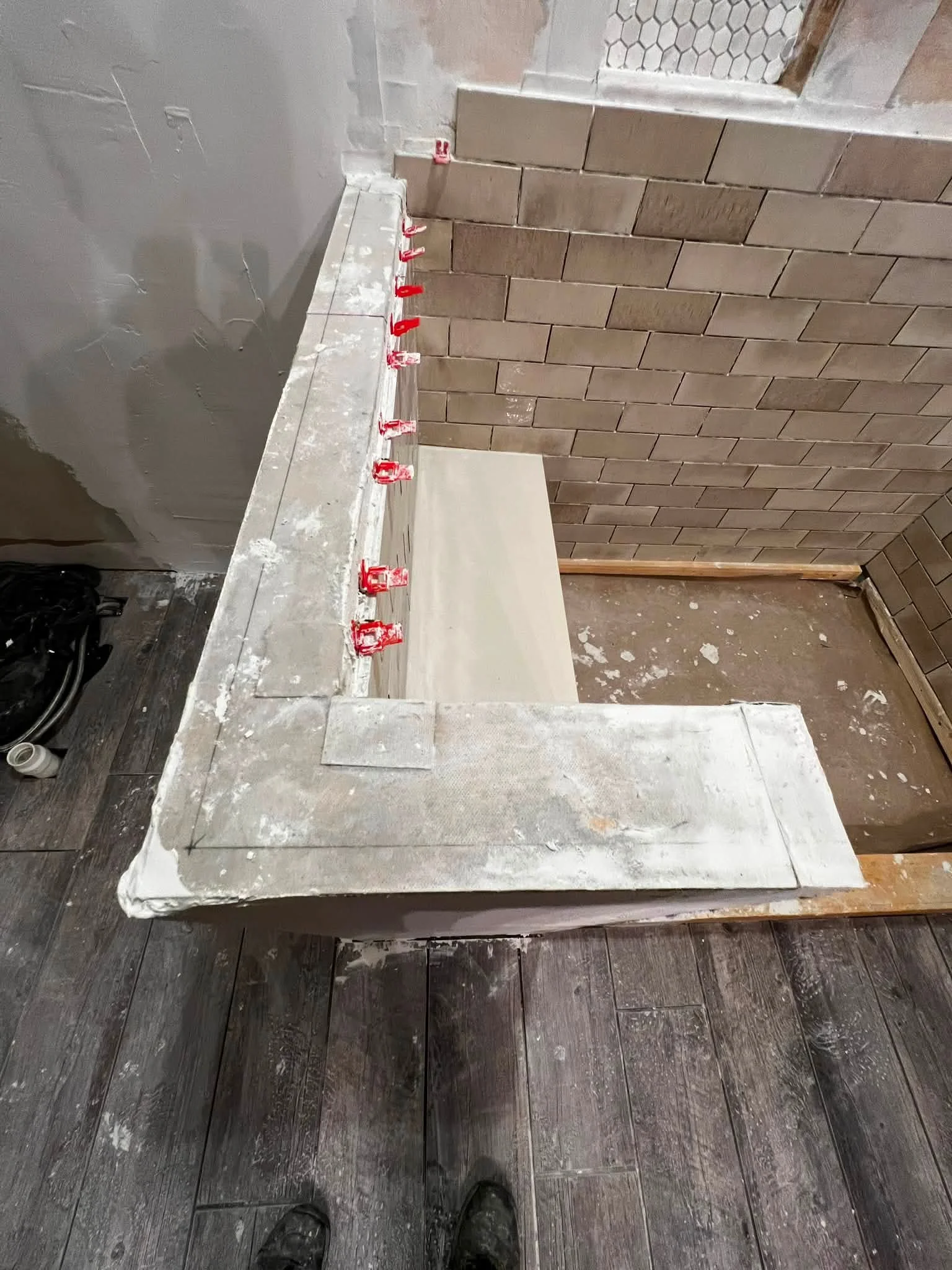 Construction site with a workbench, brick wall, and wood flooring. Red clamps attached to the workbench, and construction materials scattered around.