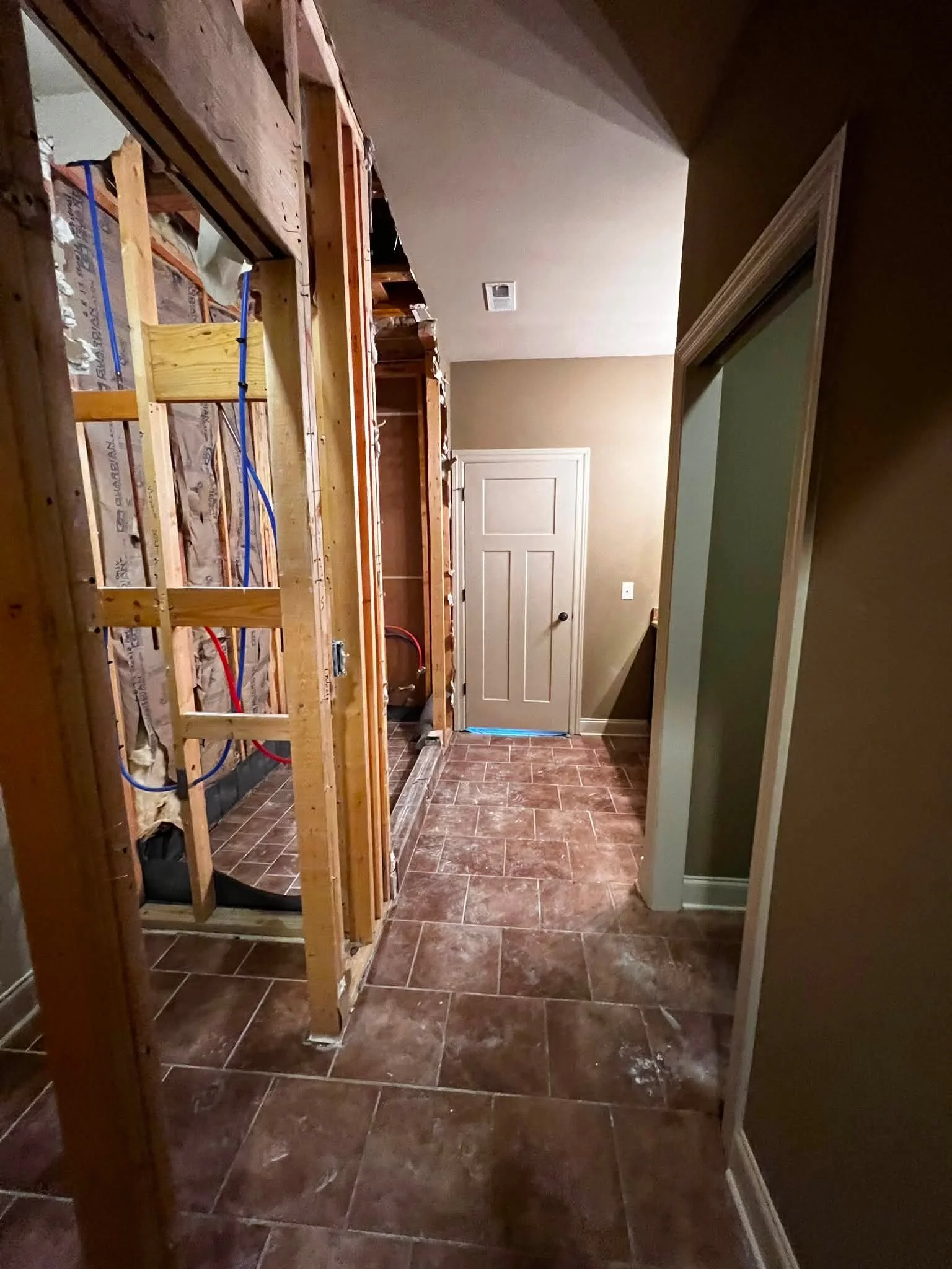 Interior space under renovation with exposed wooden framing, a closed doorway, and brown tiled flooring.