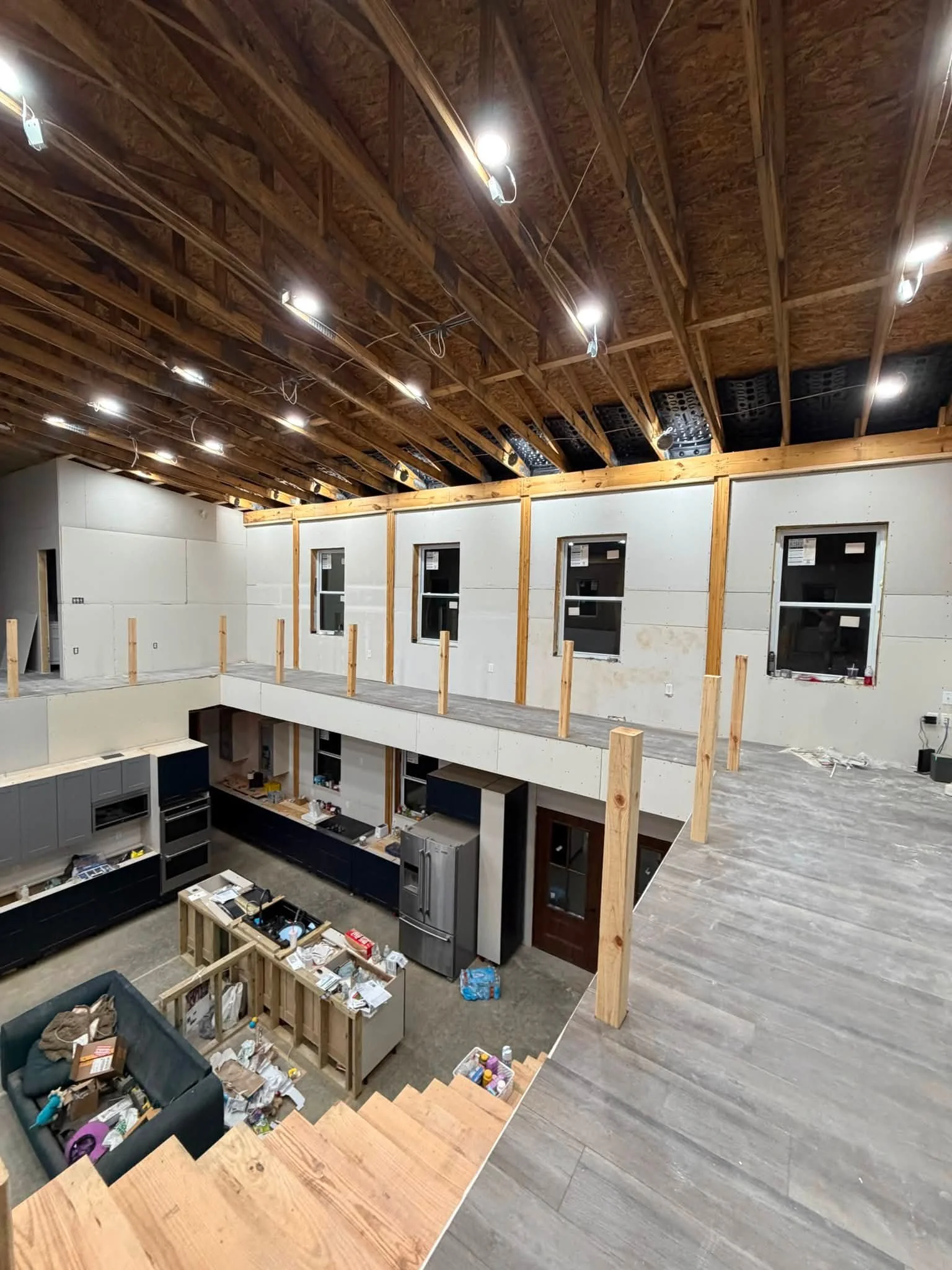 Interior of a house under construction with exposed wooden beams on the ceiling, wall framing, and floors, with kitchen cabinets and appliances partially installed on the lower level.