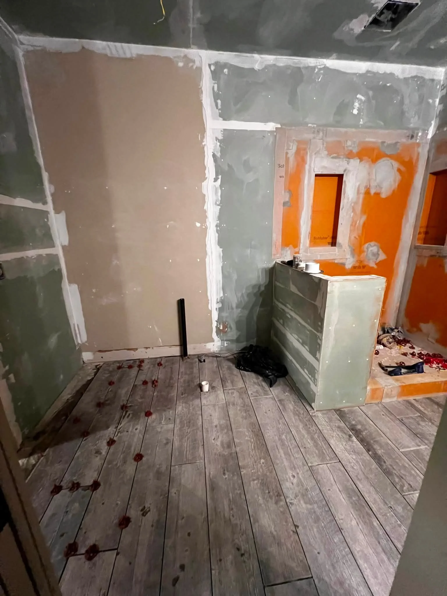 A room under renovation with unfinished walls and flooring, construction materials, and tools scattered around.