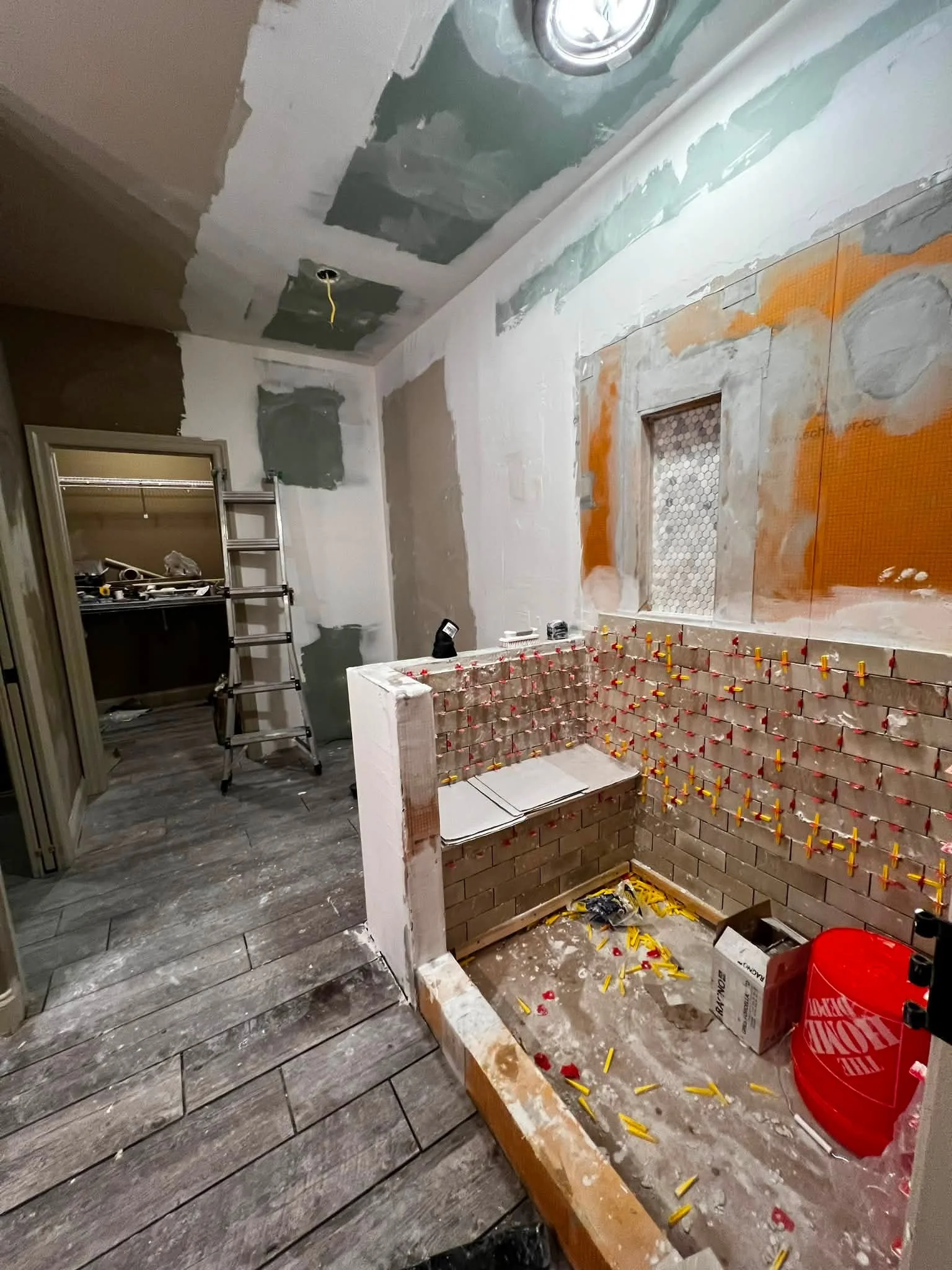 A room under renovation with unfinished walls, a partially built brick structure, a ladder, construction tools, and scattered building materials.