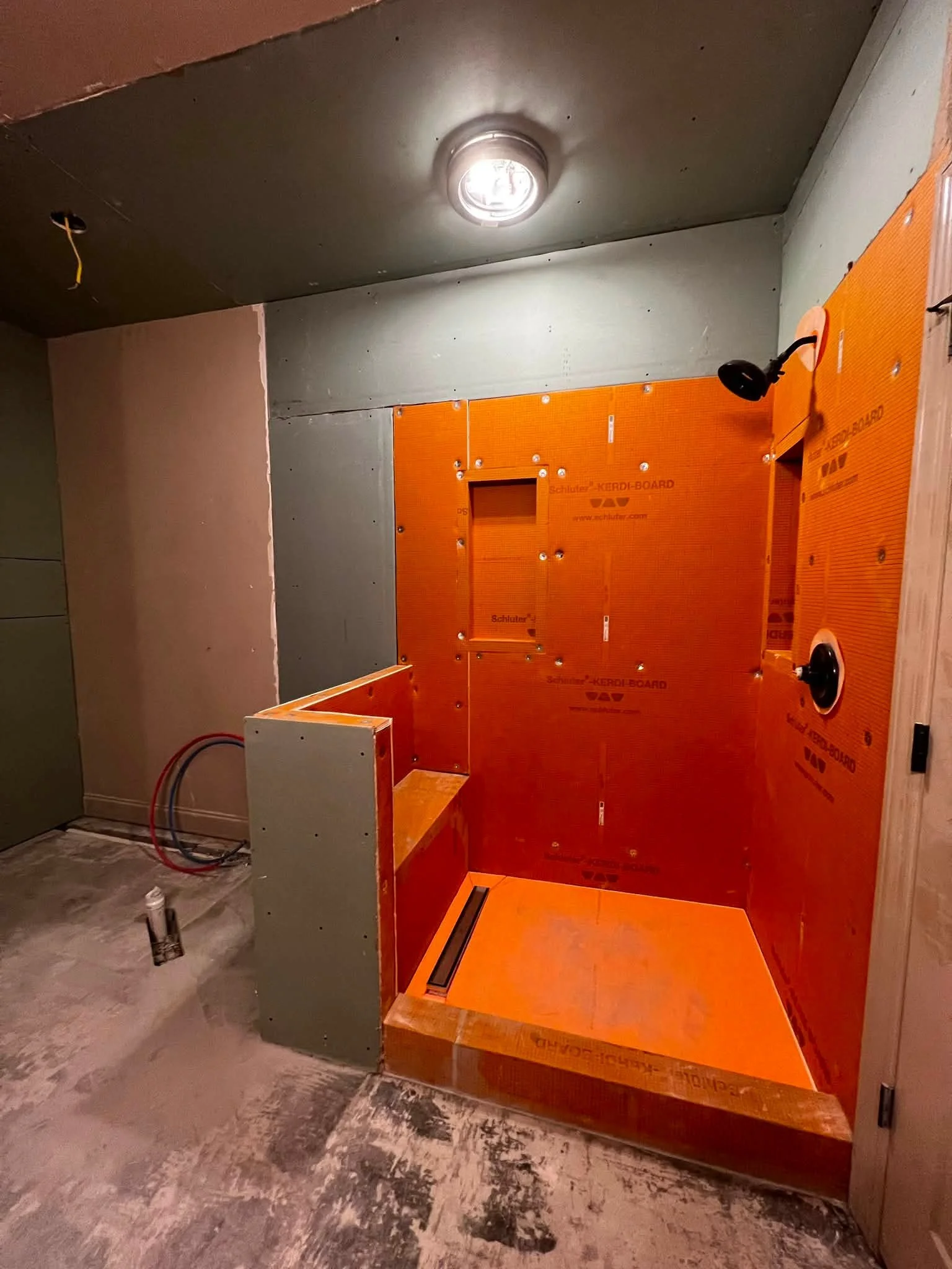 An unfinished bathroom or utility room with exposed drywall and subfloor. There are no fixtures installed yet, but electrical outlets, wires, and plumbing pipes are visible. The area appears under construction or renovation.