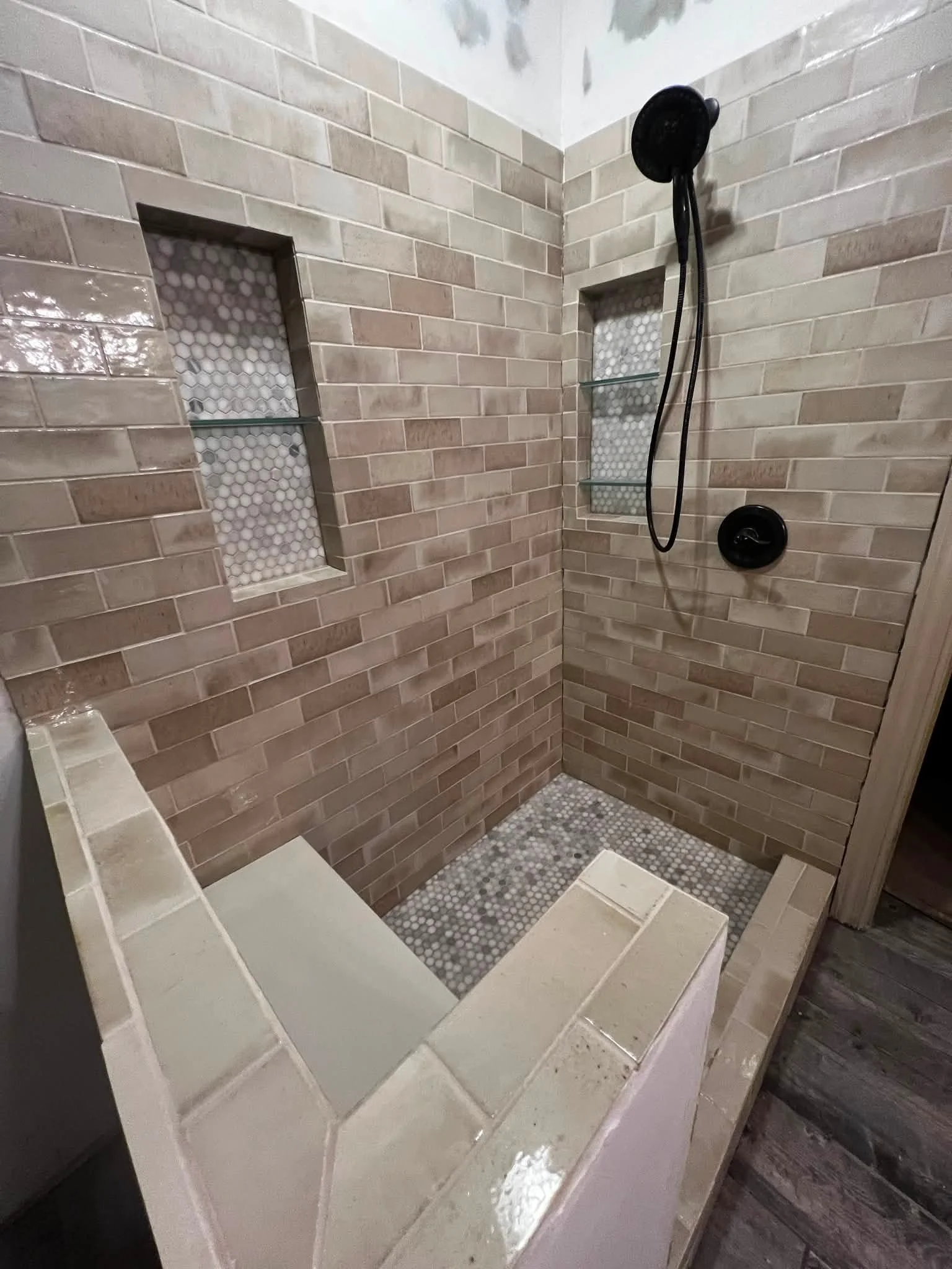 A tiled shower area with beige subway tiles on the walls, a small built-in niche with hexagon mosaic tiles, and a showerhead with a handheld spray attached to the wall.