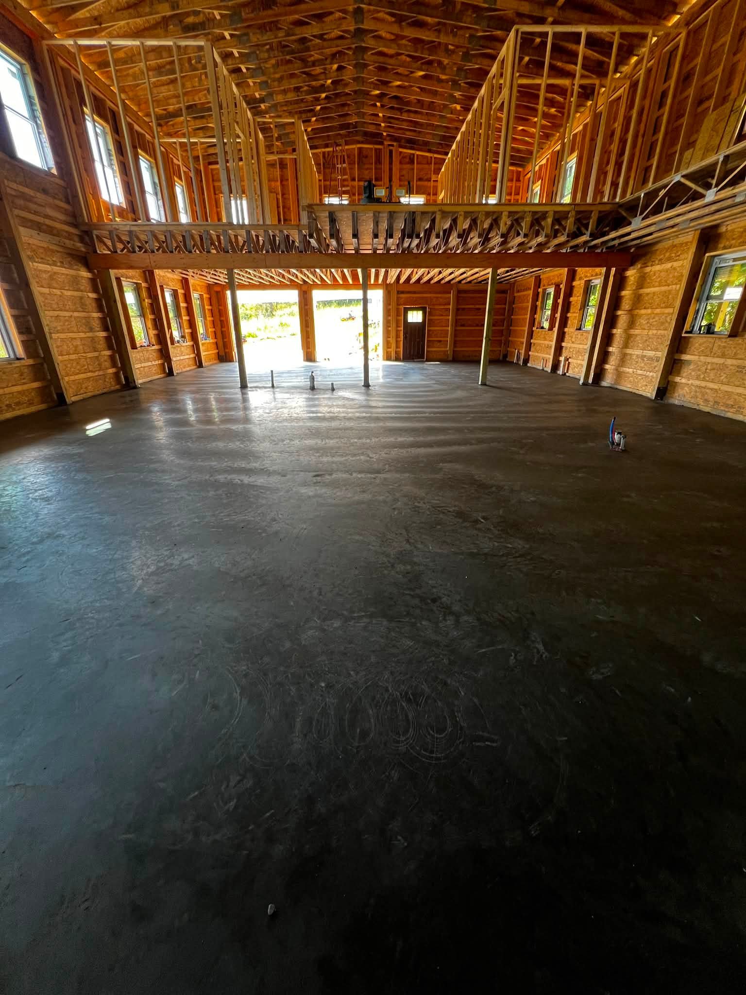 Interior view of a house under construction with exposed wooden framing and a concrete floor.
