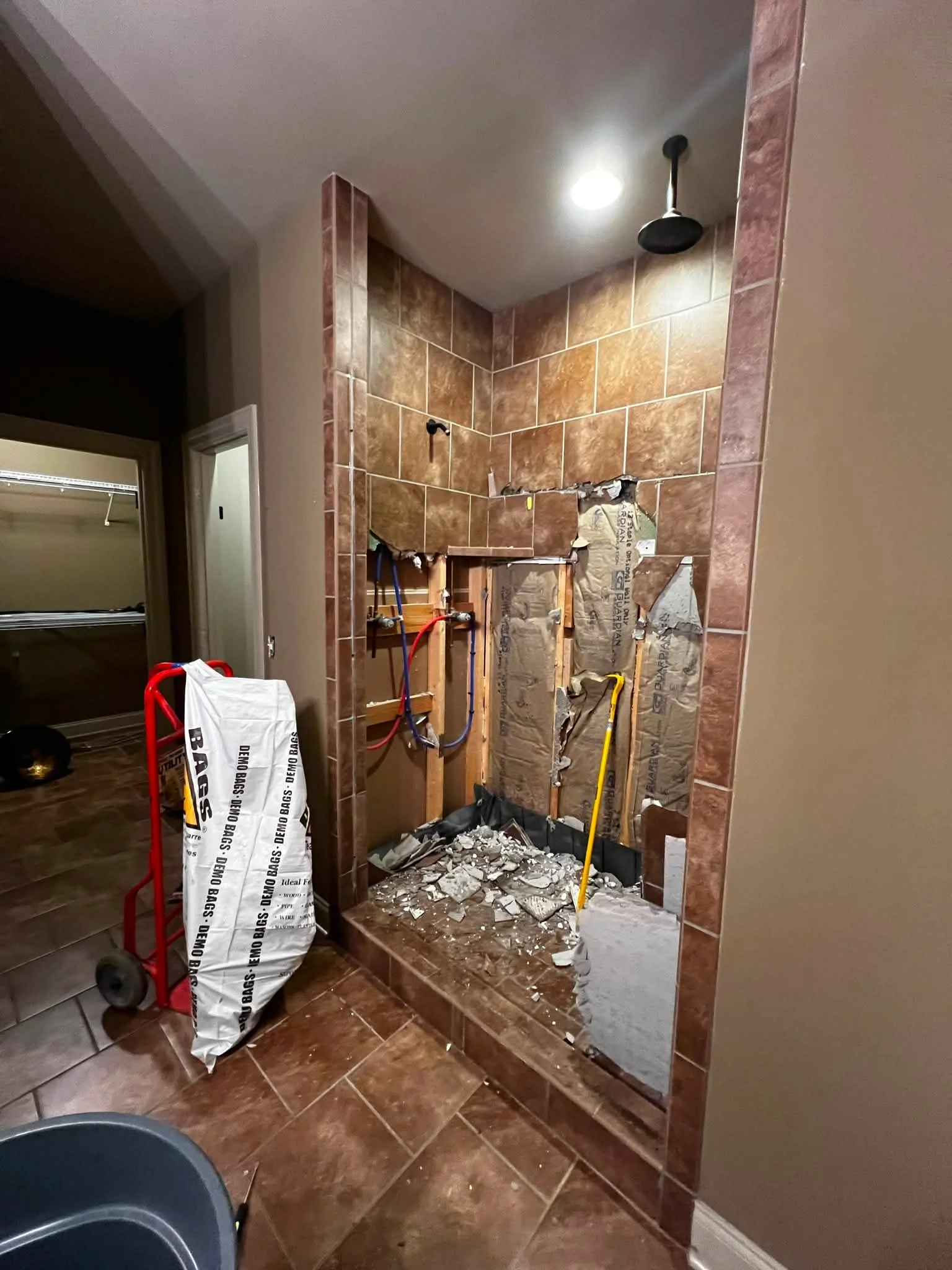 Bathroom under renovation with tiled wall, exposed pipes, construction debris, and tools.