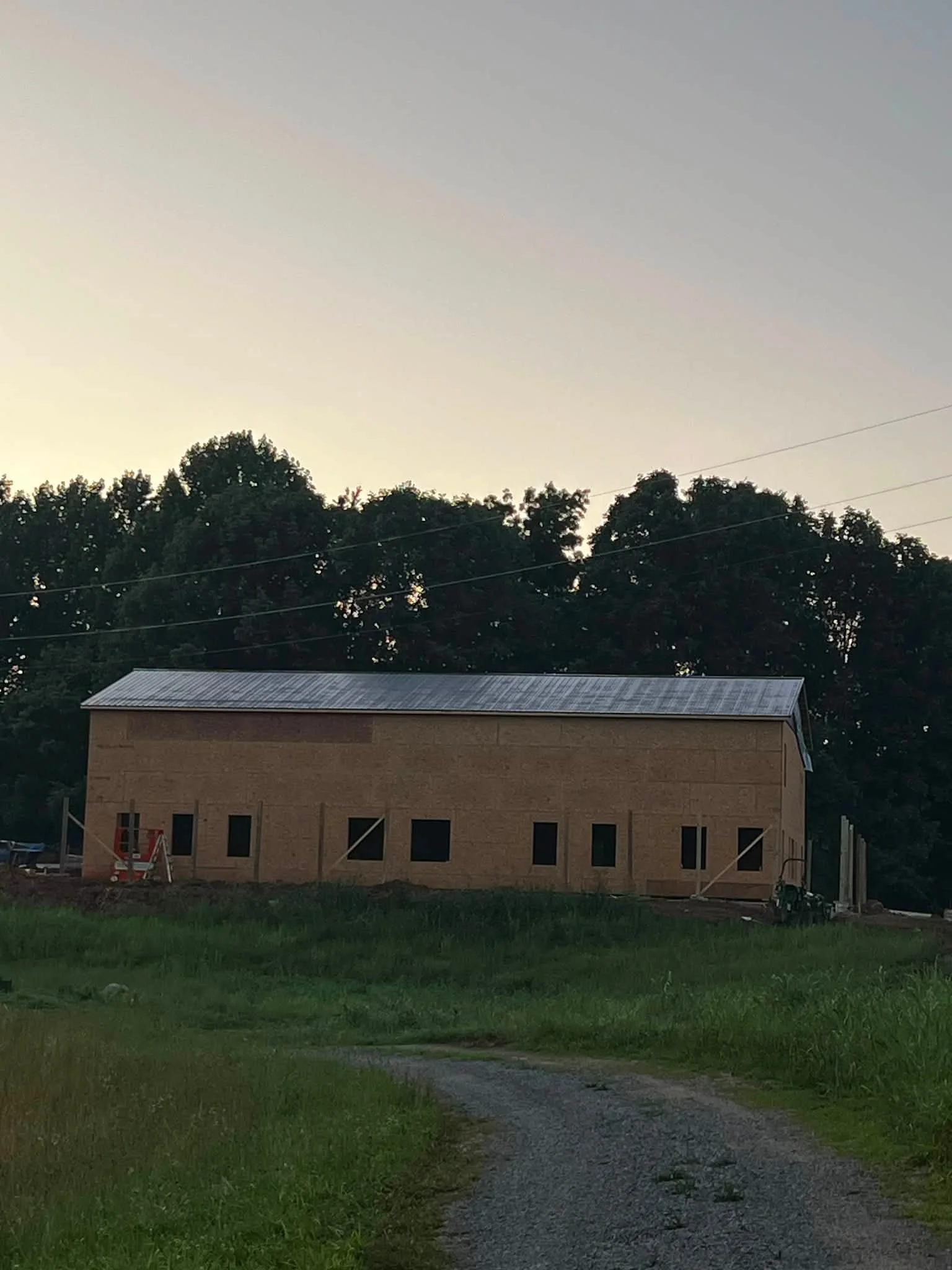 A house under construction with a metal roof, surrounded by green grass and trees, at dusk.