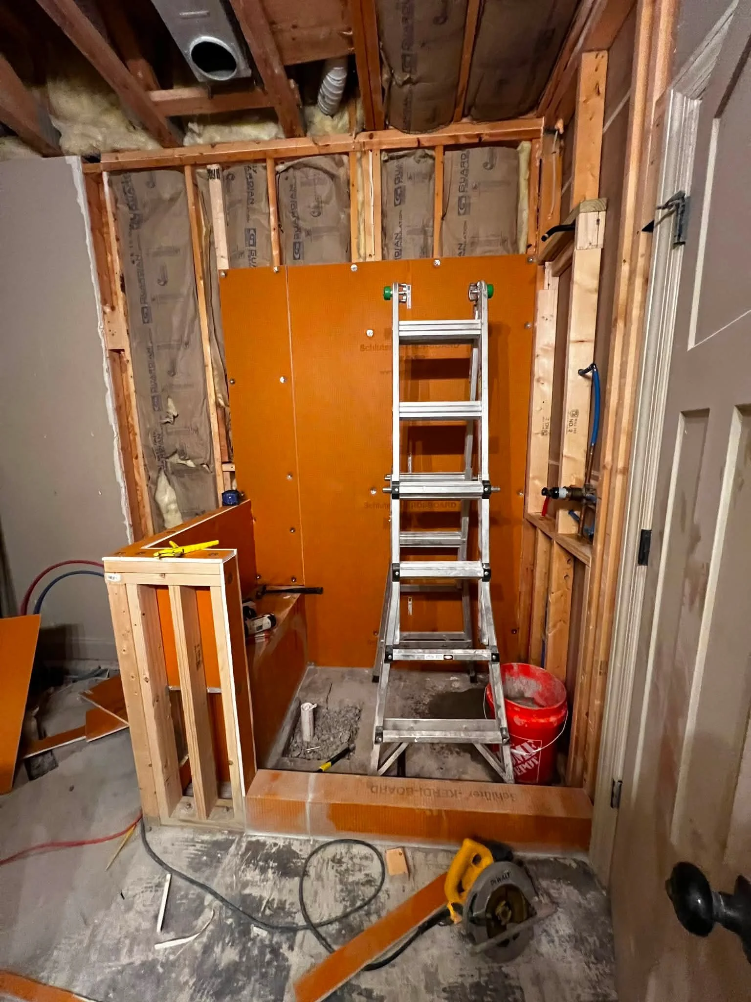 Construction workspace with a partially built wall, a ladder, tools, and insulation materials in a garage or basement.