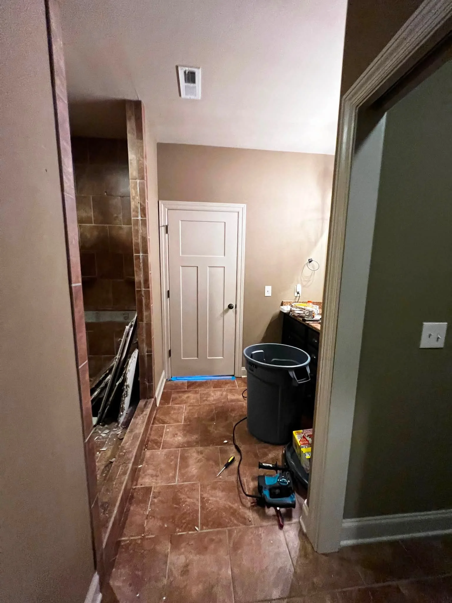 A small kitchen or laundry area with a doorway, a trash can, and tools on the floor, possibly during a renovation or repair.