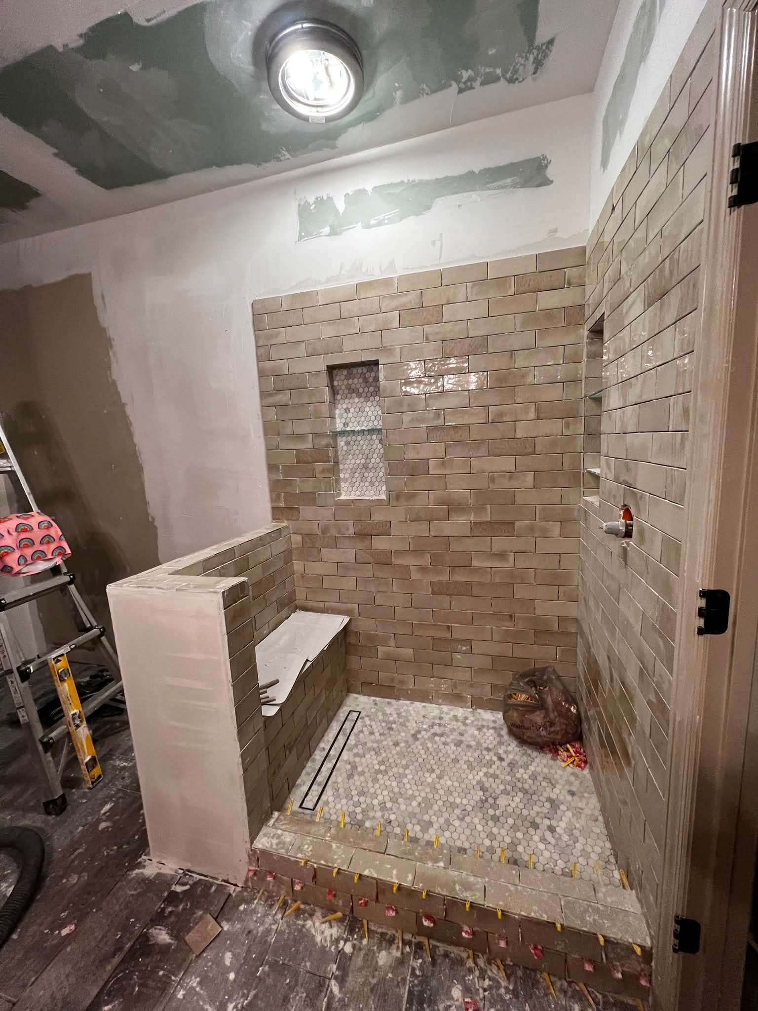 A bathroom with partially finished brick wall tiles and mosaic tile flooring, with construction materials and tools present.