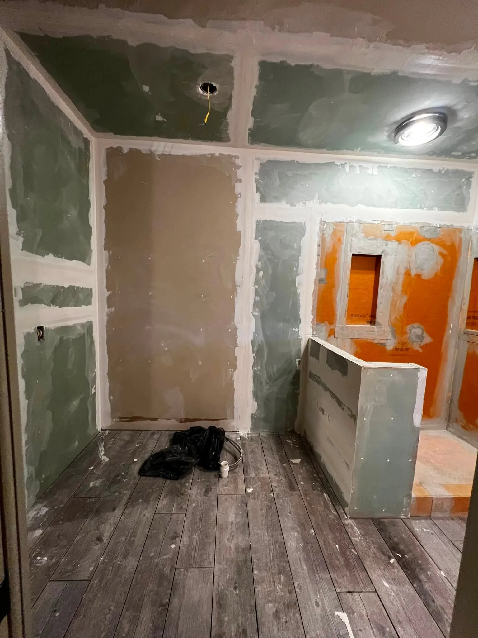 Room under construction or renovation with drywall partially installed, a wooden floor, and construction supplies on the floor.