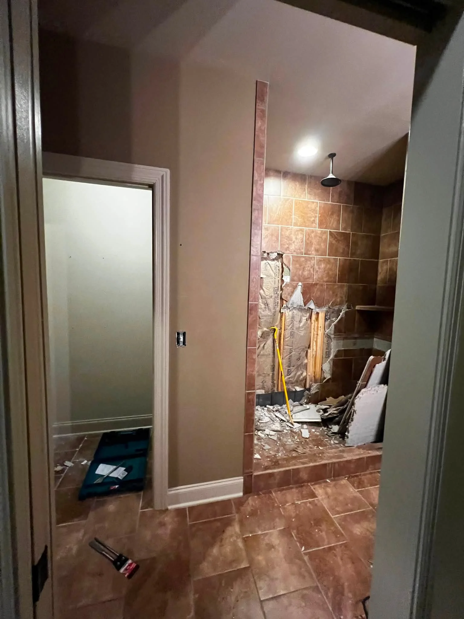 Bathroom under renovation with tiles on the floor and walls, some construction debris, and tools like a level and a hammer. An open closet with a mirror is visible in the foreground.