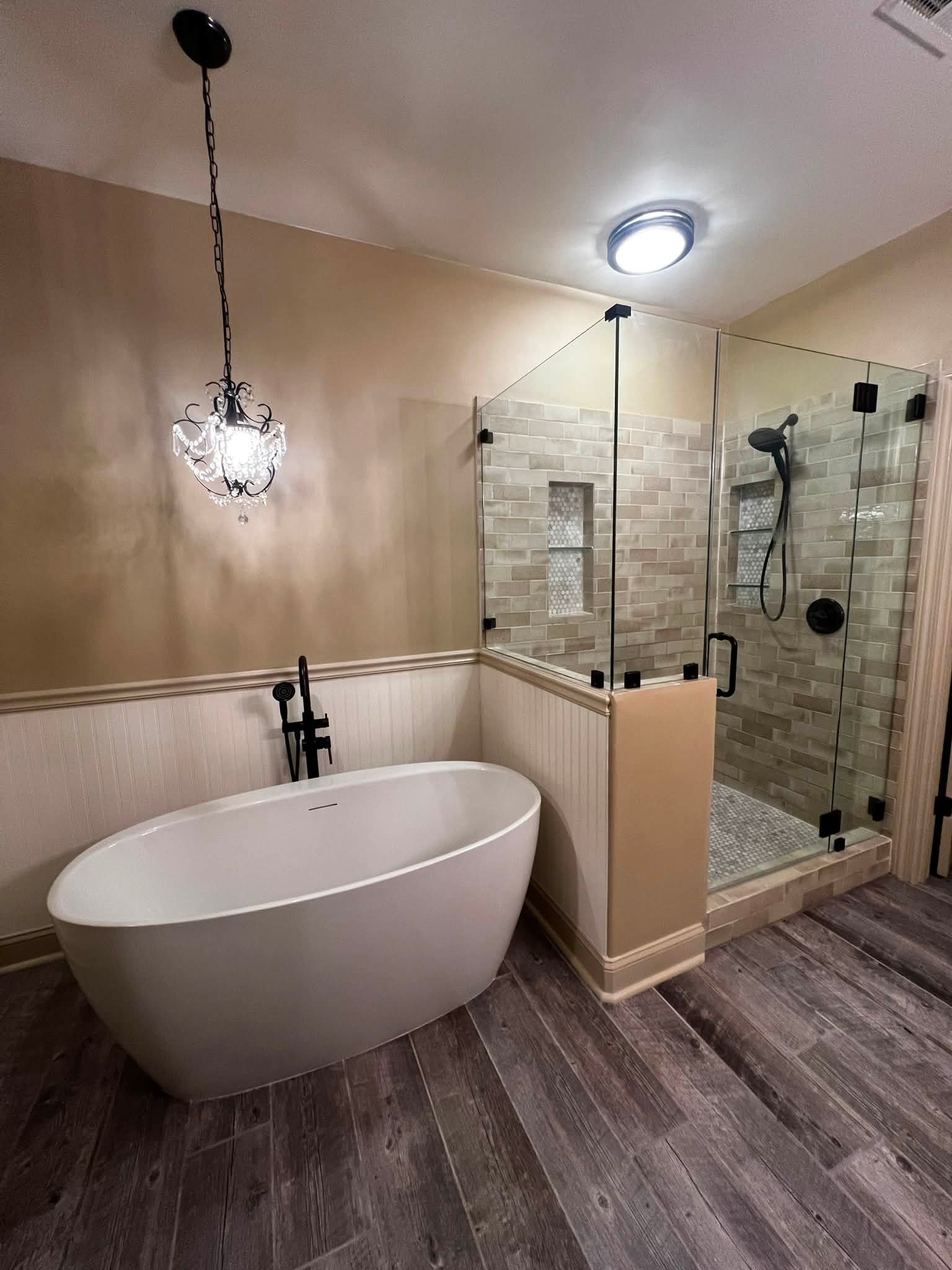 Modern bathroom featuring a standalone bathtub, a glass-enclosed shower with brick tile walls, and a decorative chandelier-style light fixture.