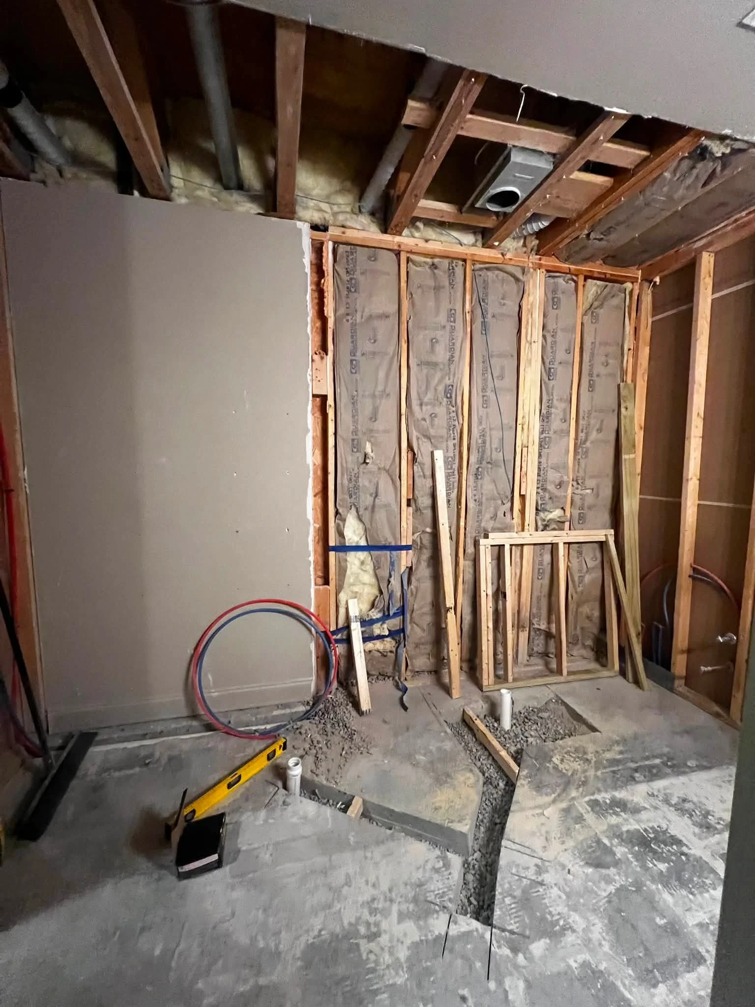Interior of a room under construction with exposed wooden studs, insulation, and plumbing pipes, ready for drywall installation.