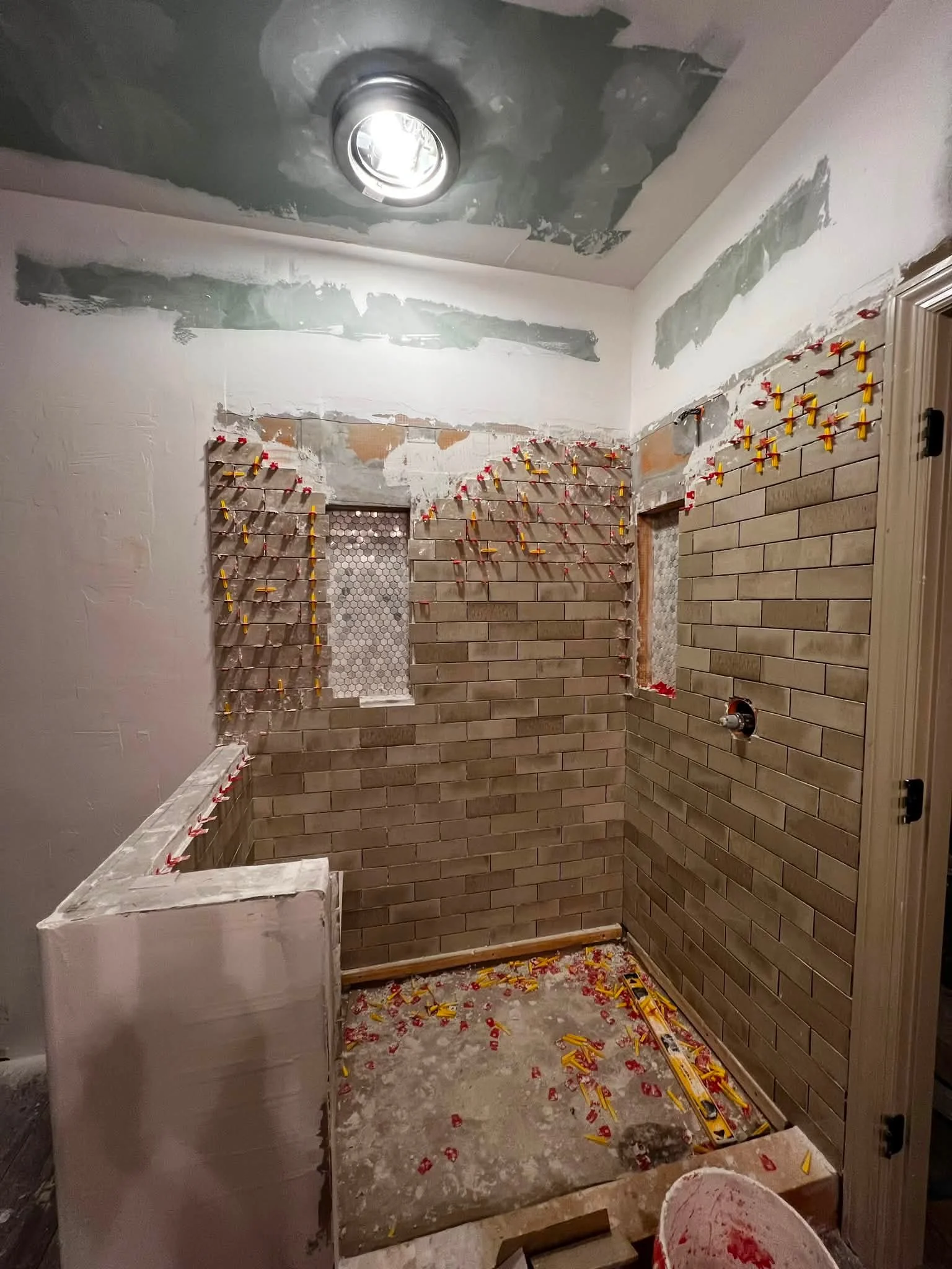 A bathroom in the process of being renovated, with brick wall tiles being installed, construction clips holding the tiles in place, and construction debris on the floor.