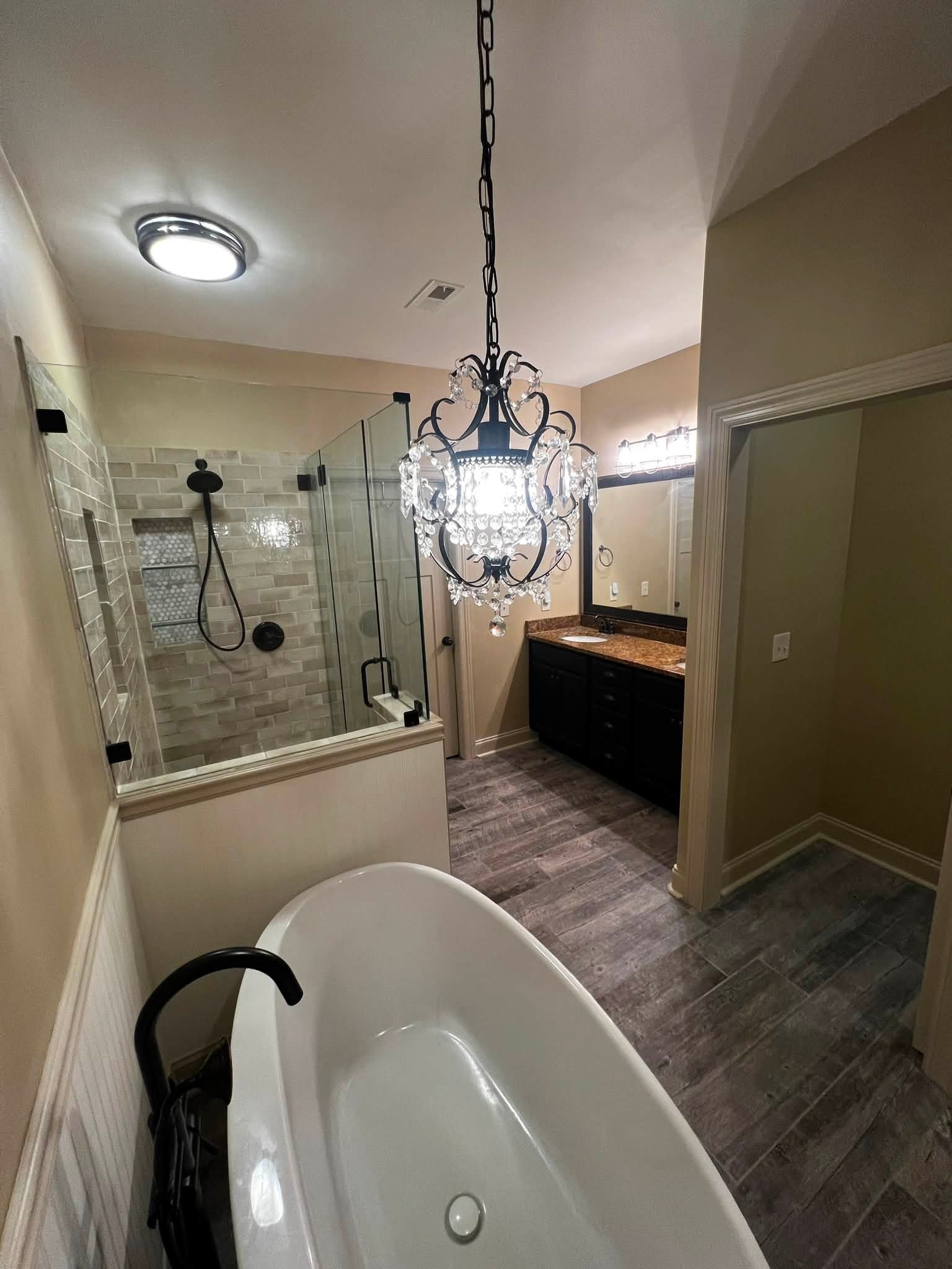 Bathroom with a large corner shower, chandelier hanging from the ceiling, vanity with a granite countertop, and a bathtub in the foreground.