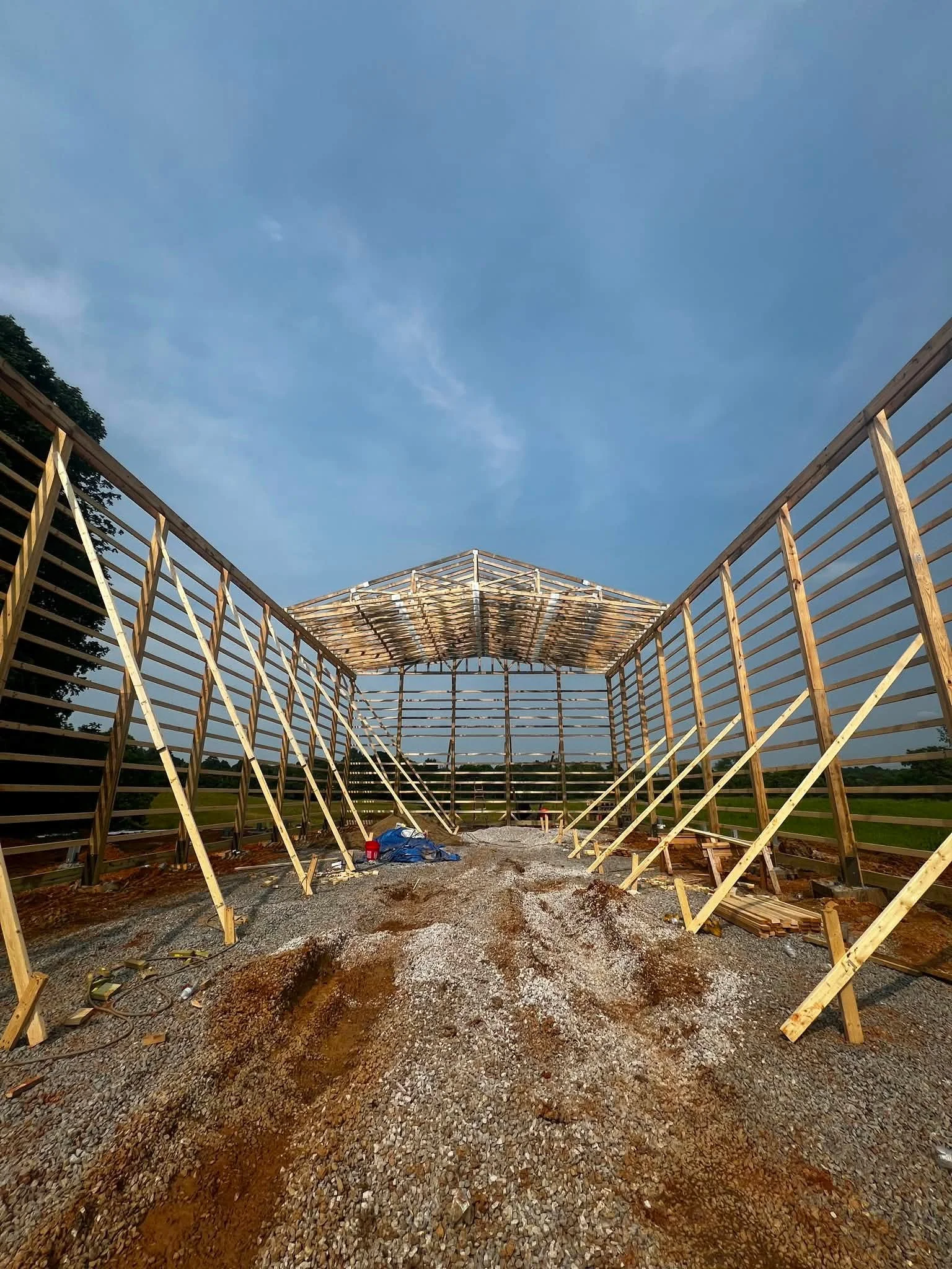 Wooden framework of a building under construction with a blue sky overhead and trees in the distance.