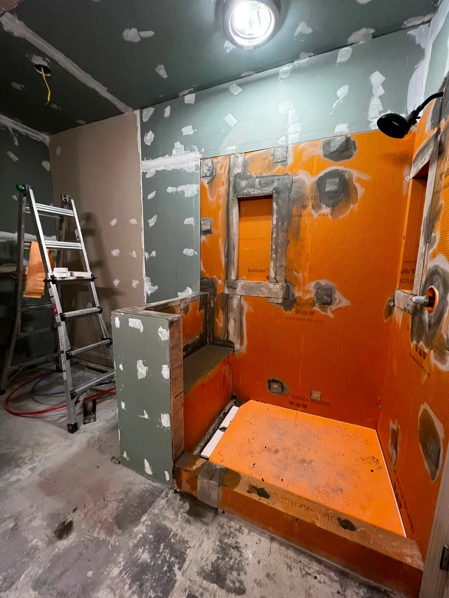 Room under construction with drywall in progress, an orange insulating board, a step ladder, and construction materials on the floor.