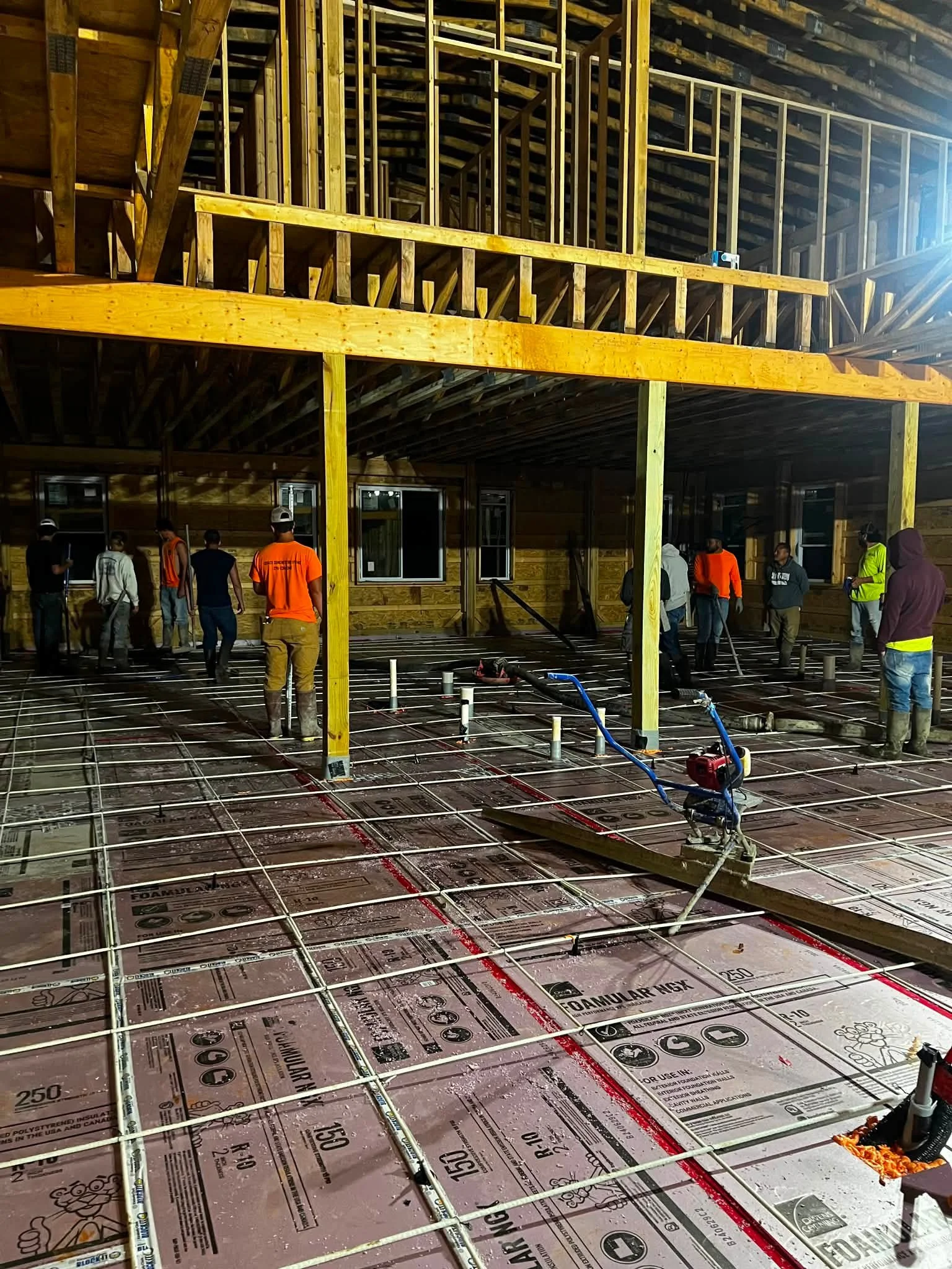 Construction site with wooden framework and steel rebar on the floor, workers in safety vests and helmets working on building the structure.