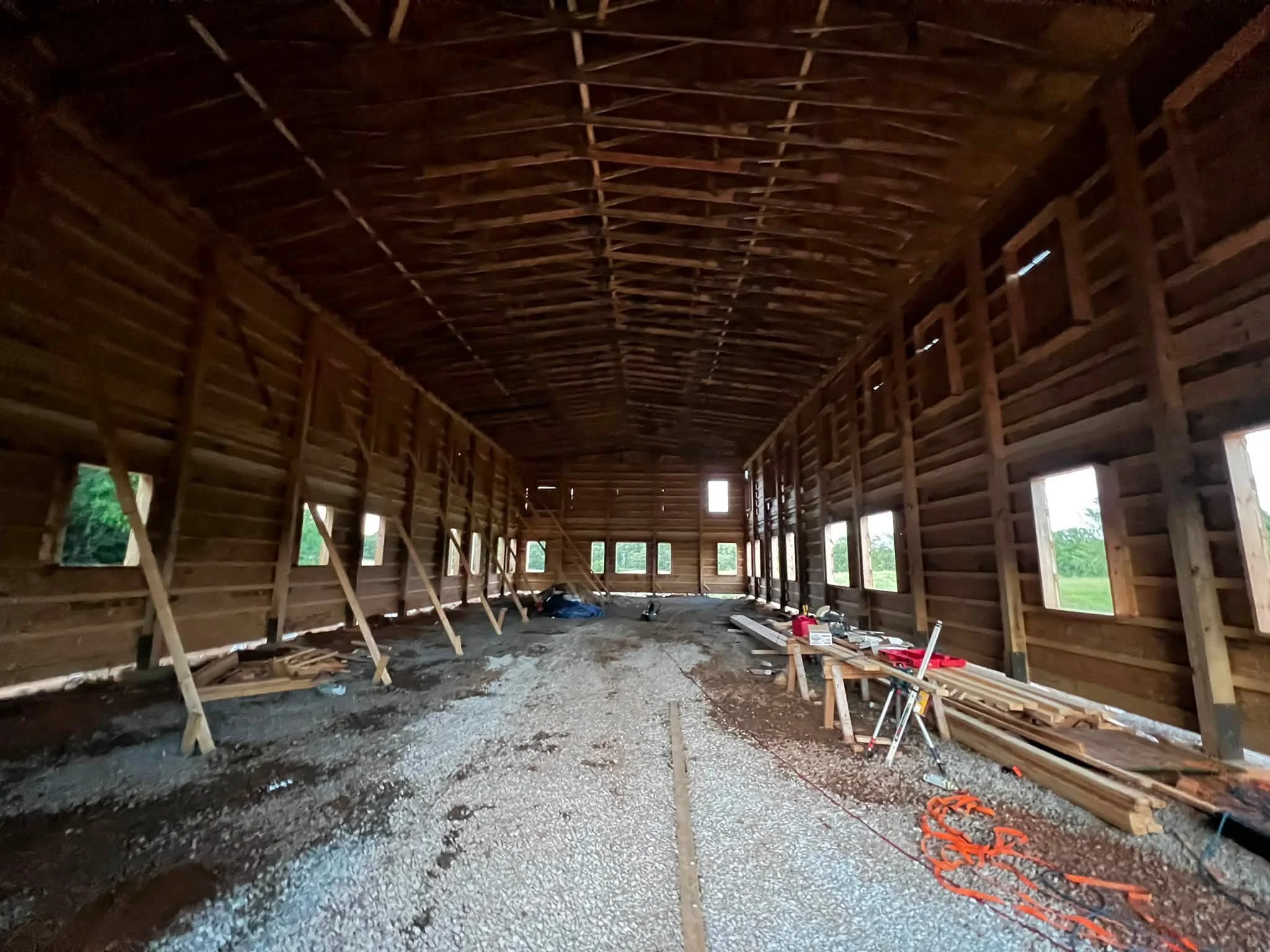 Interior of a half-built wooden structure with exposed framing, windows, and construction tools on the floor.