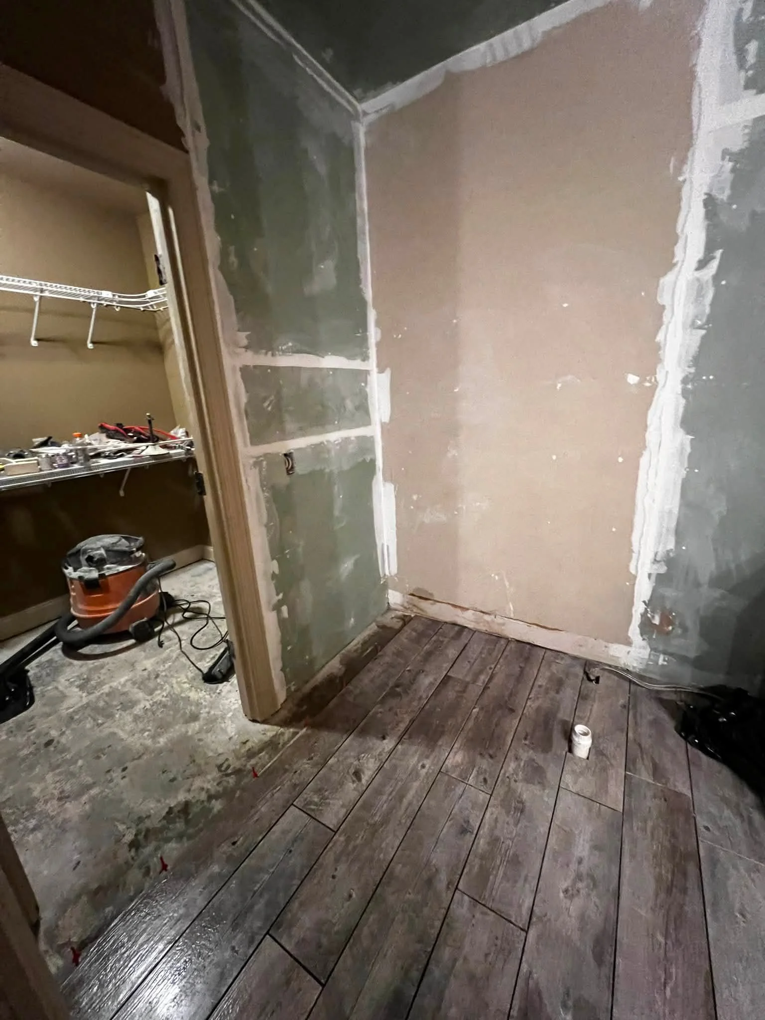 Room under renovation with partially torn drywall, exposed wiring, and new wood flooring being installed.