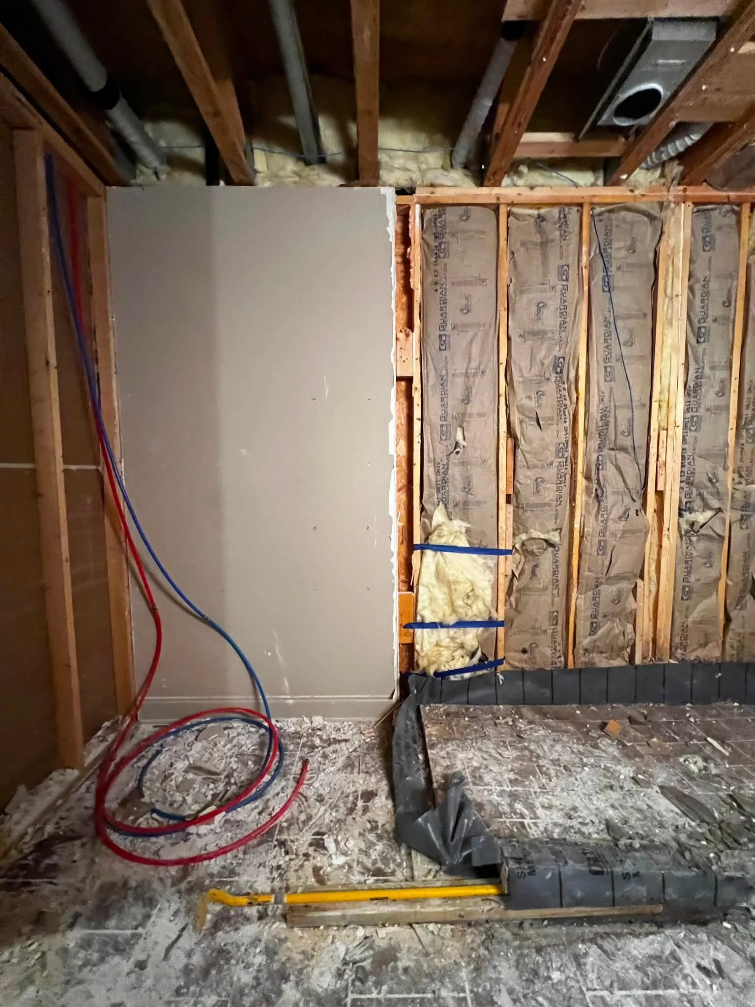 Construction site showing unfinished interior wall framing, insulation, electrical wiring, and ductwork.