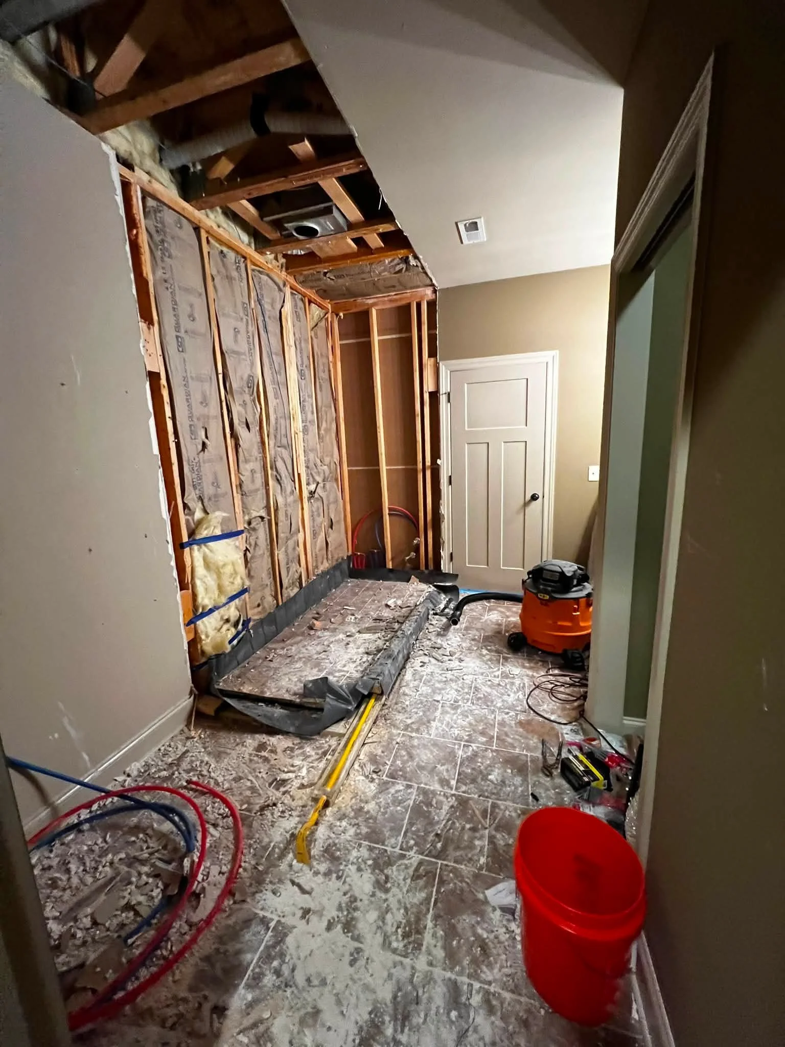 Room under renovation with exposed wooden framing, insulation, construction tools, and debris on the floor.