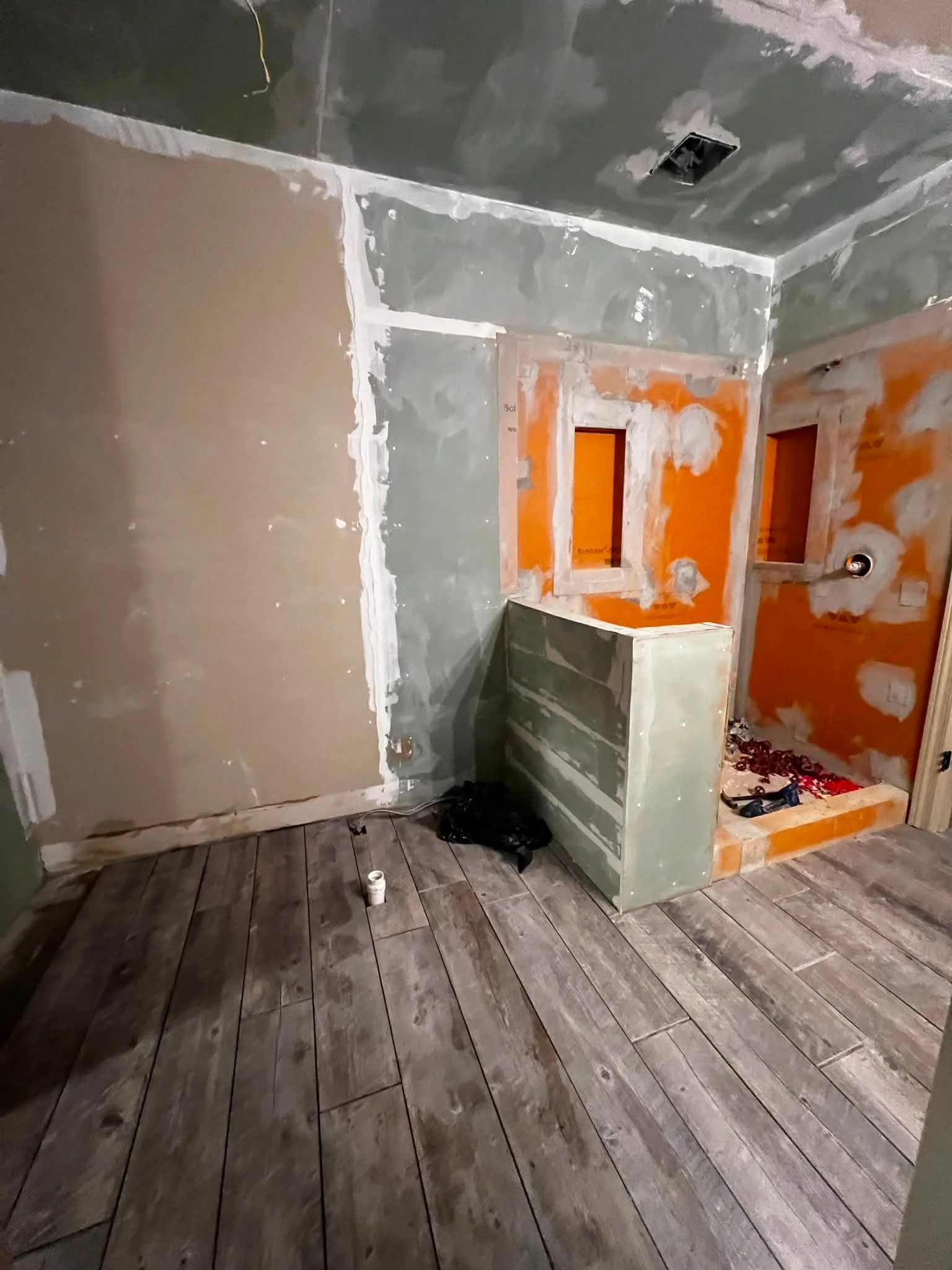 Interior of a room under construction or renovation, with drywall installed on the walls and ceiling, a partially built cabinet or shelf, and unfinished wood flooring.