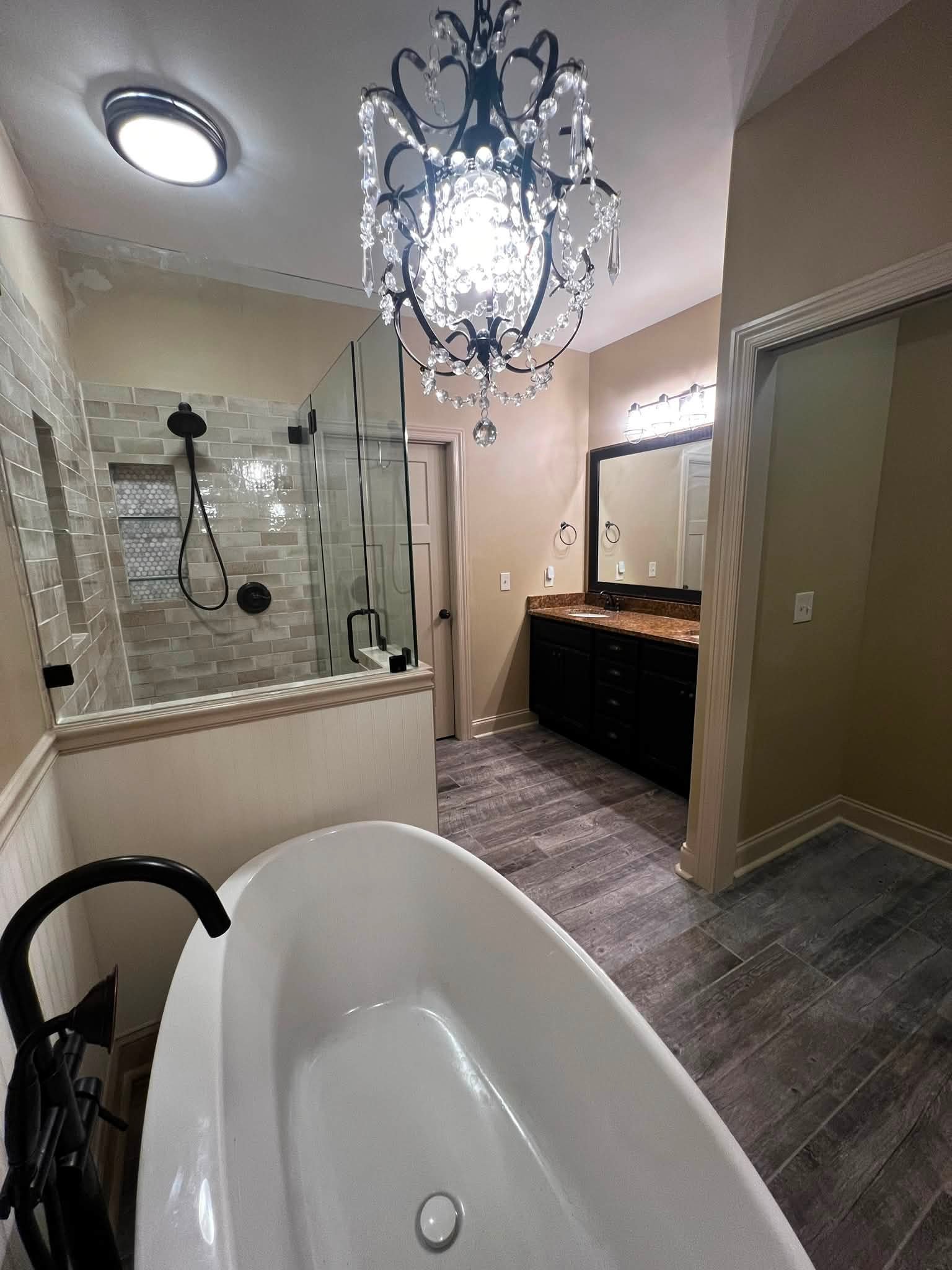 Bathroom with a clawfoot bathtub, a chandelier hanging from the ceiling, a glass-enclosed shower, a dark wood vanity with a granite countertop, a mirror, and light fixtures.