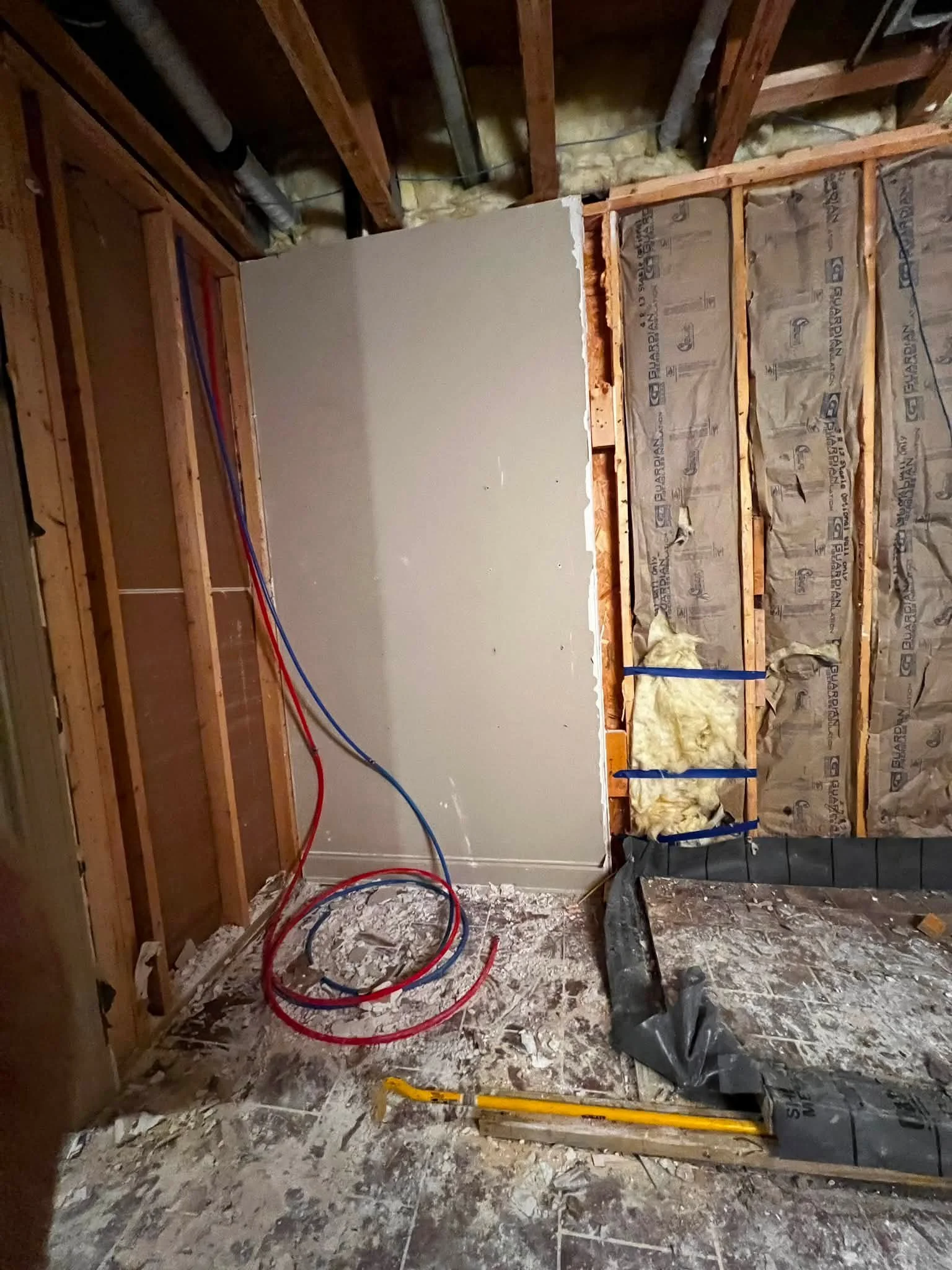 Interior of a building under construction, showing exposed wooden framework, insulation, electrical wiring, and partially installed drywall.