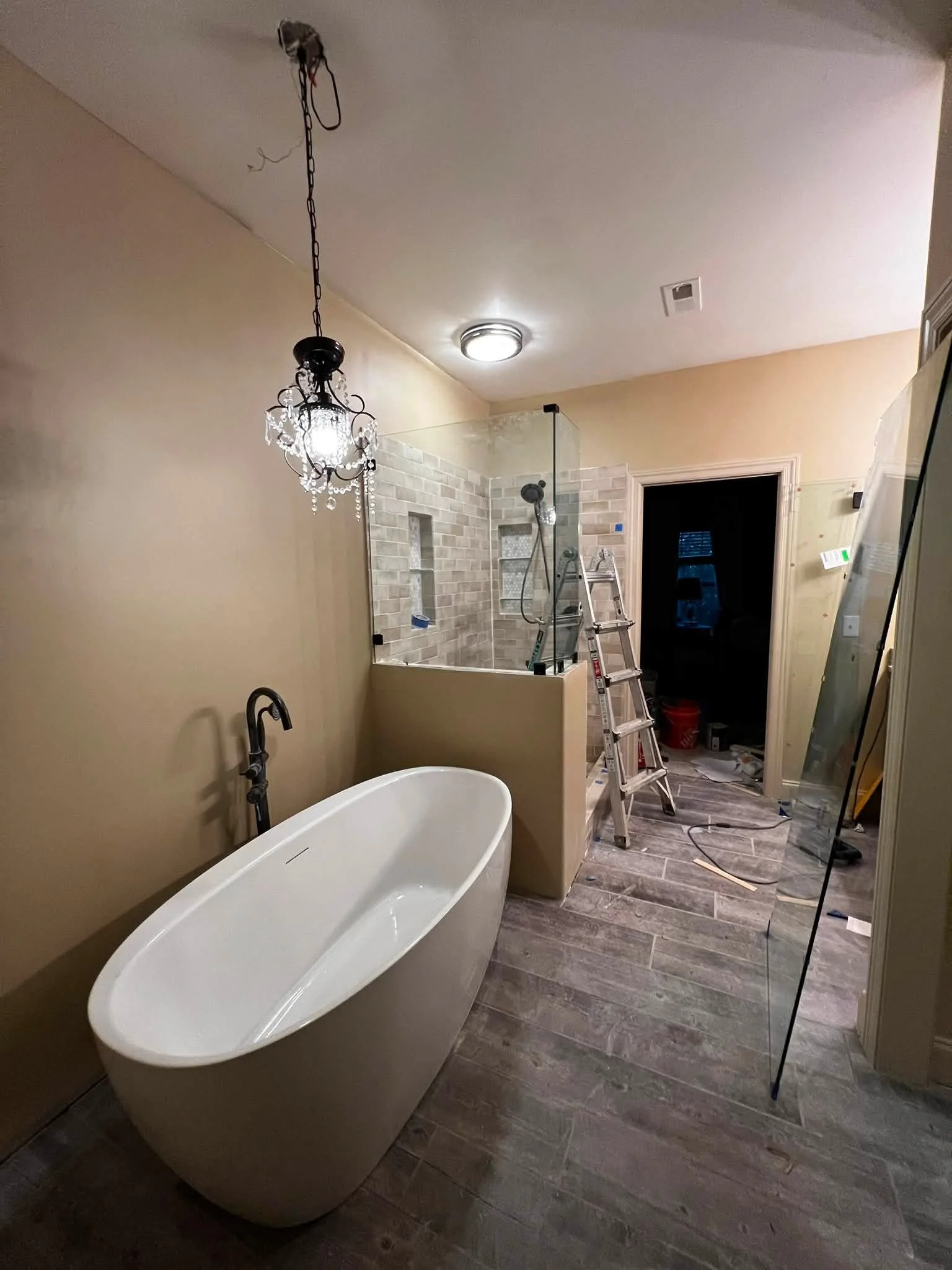 Bathroom under renovation with a freestanding bathtub, a partially installed shower area with brick tiles, a ladder, and construction tools.