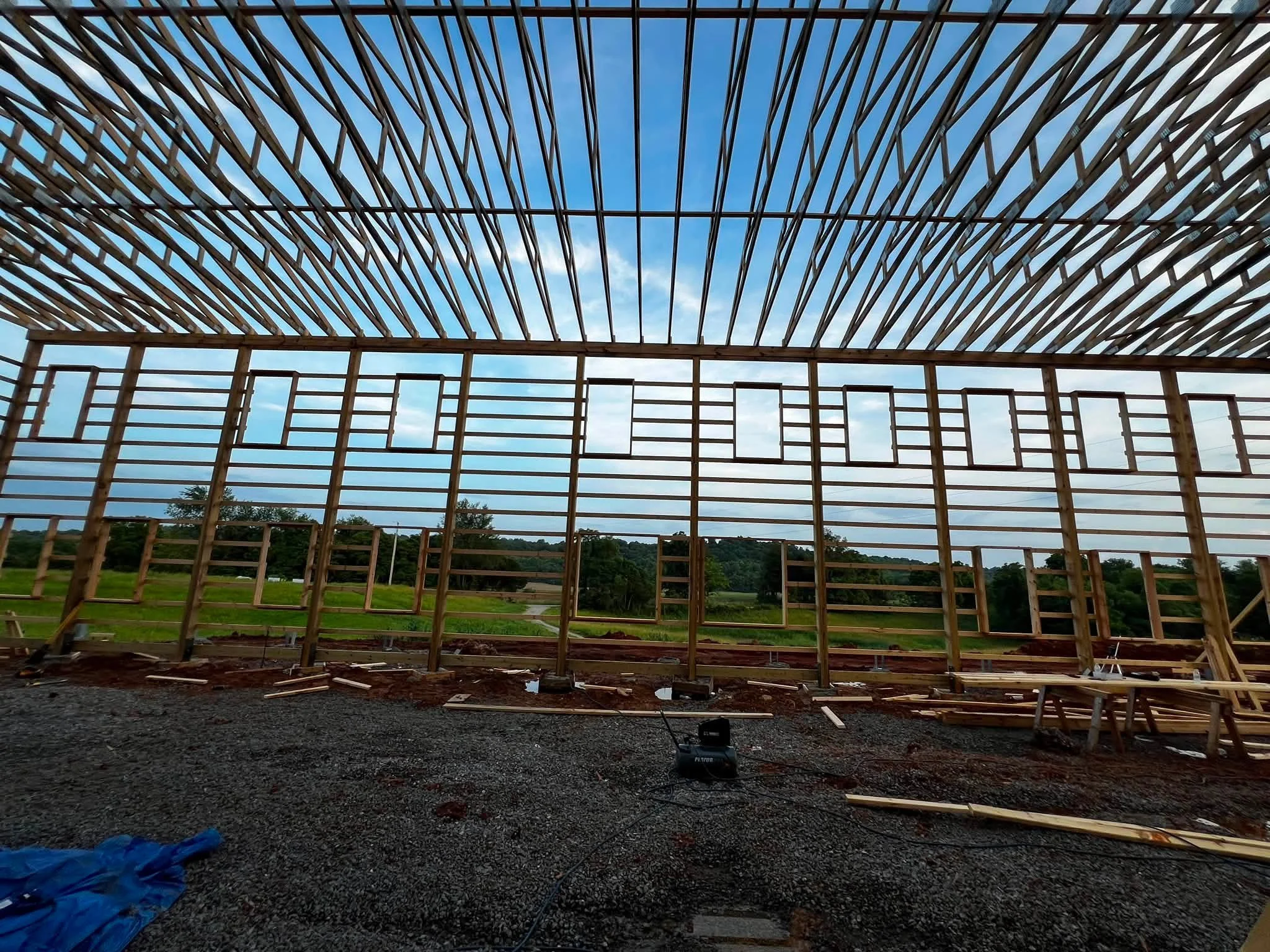 Construction site with wooden framing and a roof structure under a partly cloudy sky.