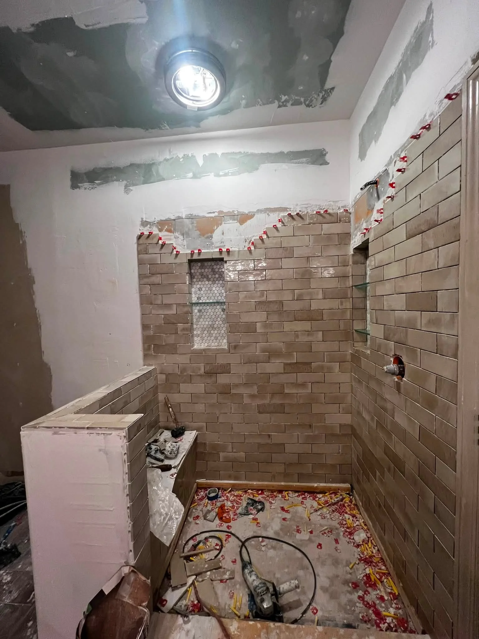 A bathroom under renovation with partially painted walls, a brick accent wall, construction tools, debris, and a patterned floor.