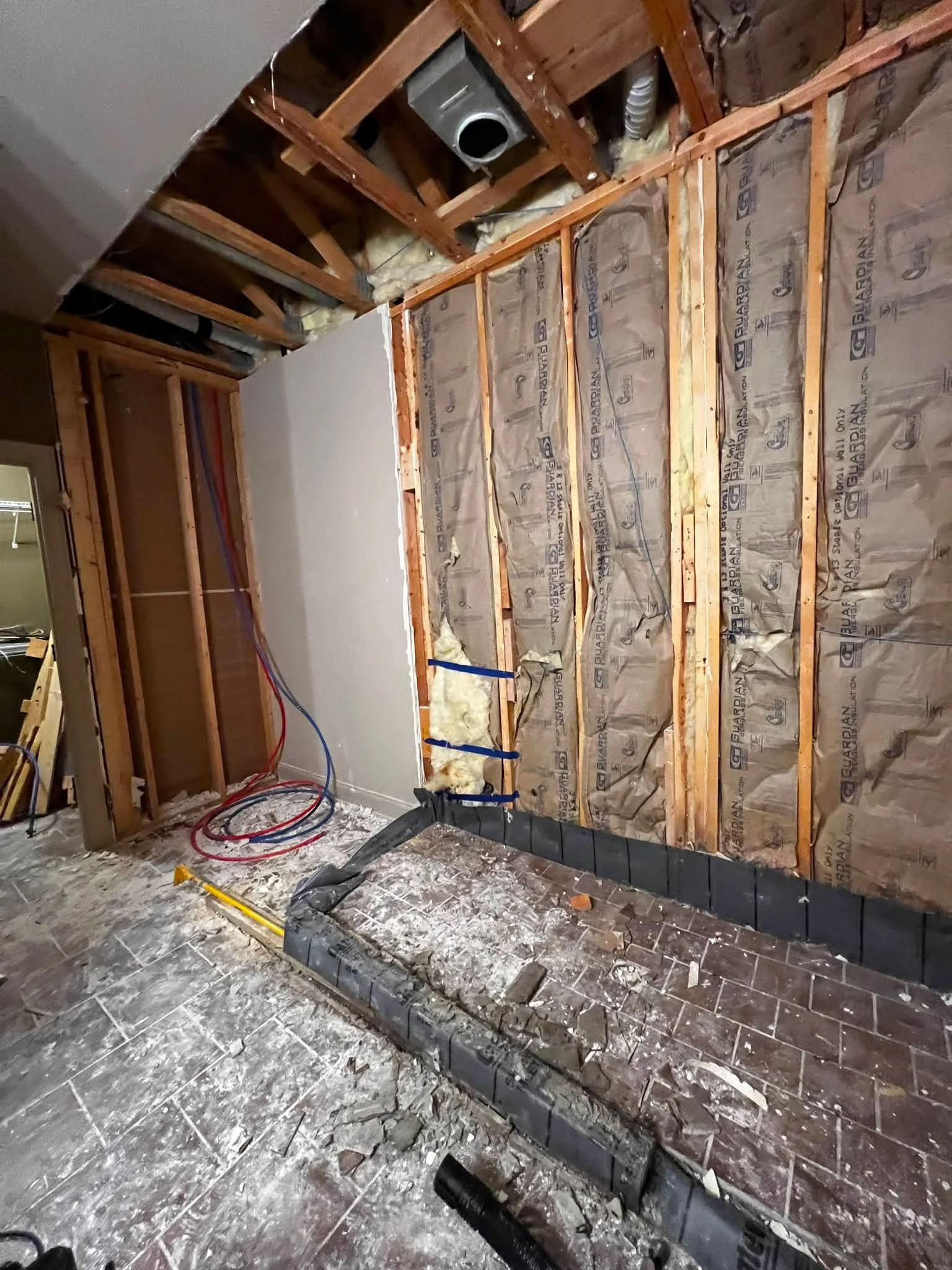 Bathroom under renovation with exposed wooden framework, insulation, plumbing pipes, and construction debris on the floor.
