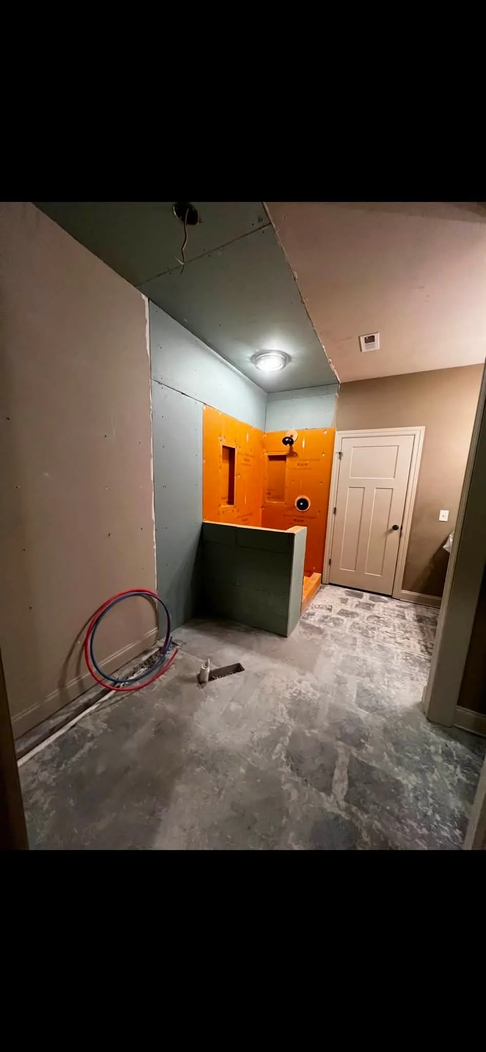 Bathroom under construction with partially tiled walls, exposed plumbing, and unfinished flooring.