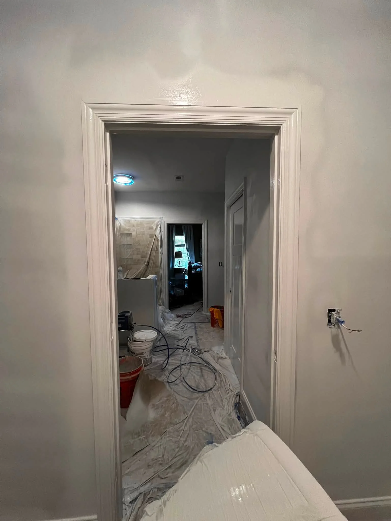 A doorway leading into a room under renovation with painter's plastic on the floor, tools, and construction materials visible inside.