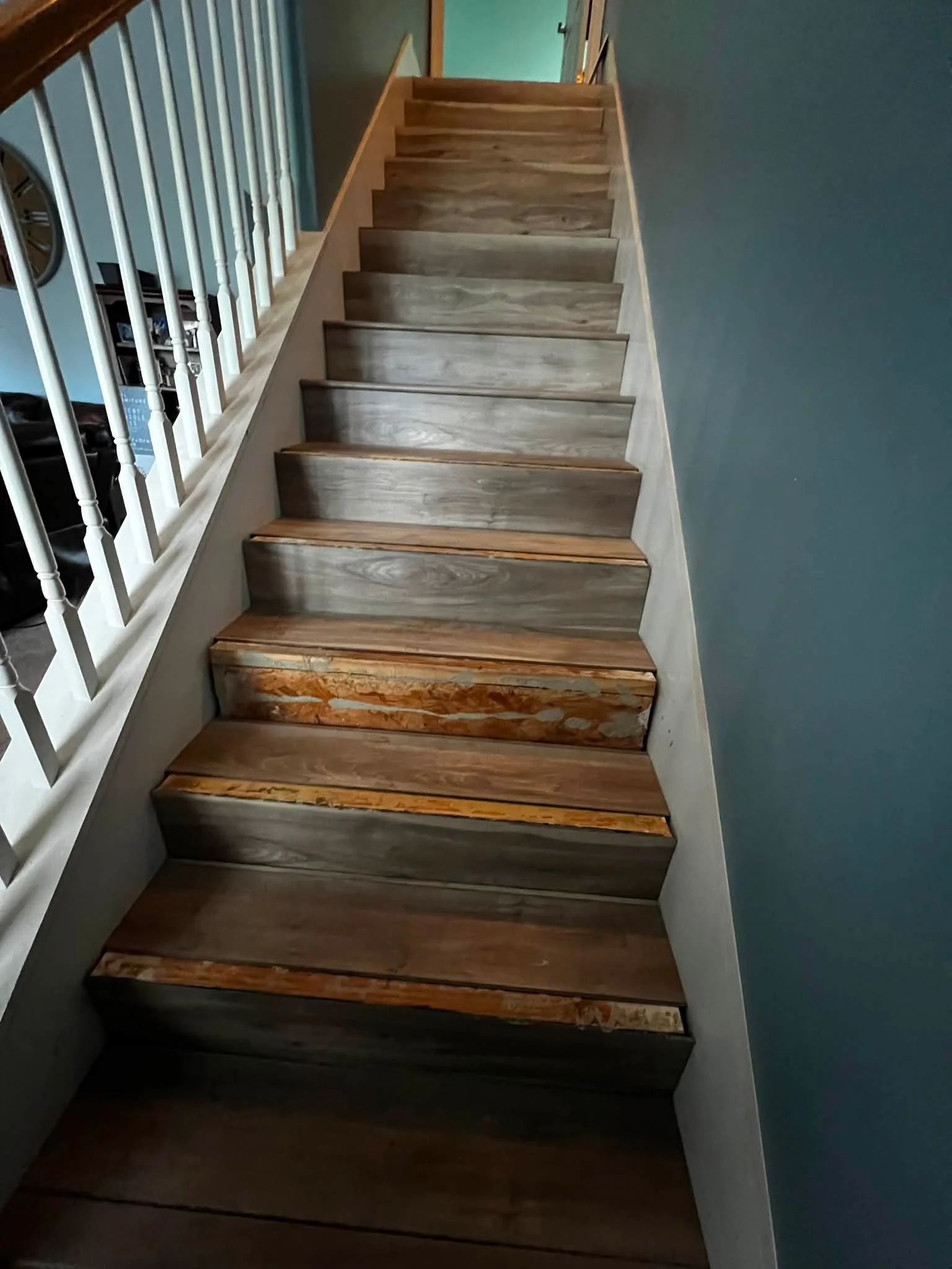 Indoor staircase with wooden treads, leading to an upper floor, with a white balustrade on the left and a teal wall on the right.