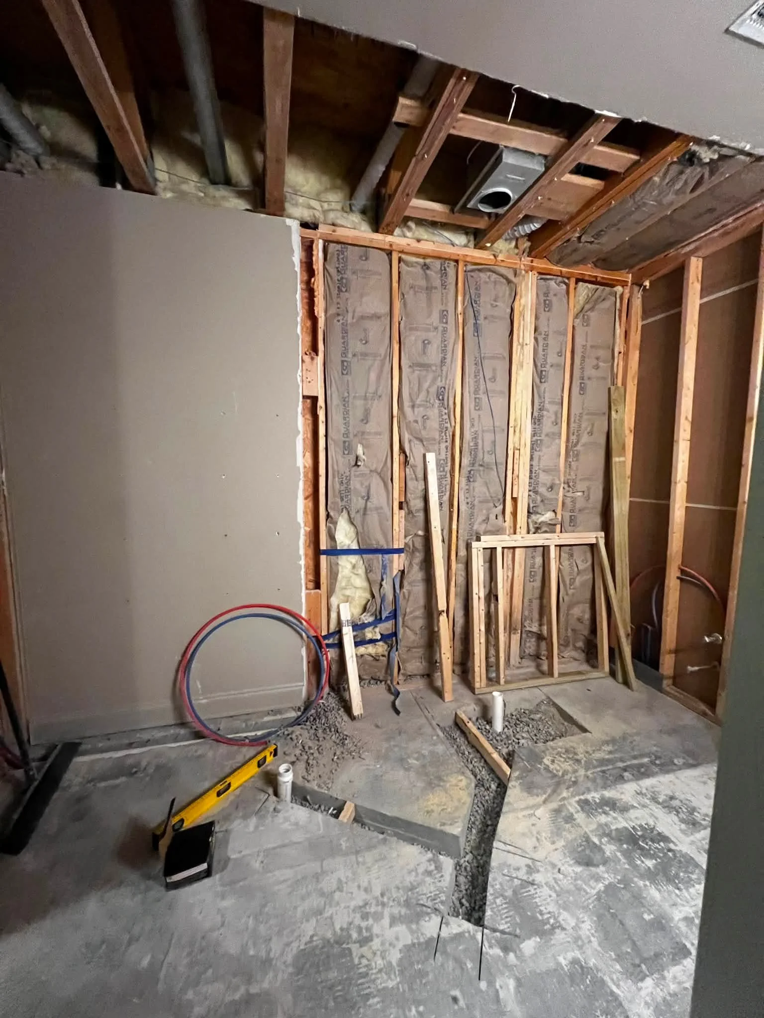 Room under construction with exposed wooden studs, insulation, and partially installed drywall. Construction tools and materials are on the floor.