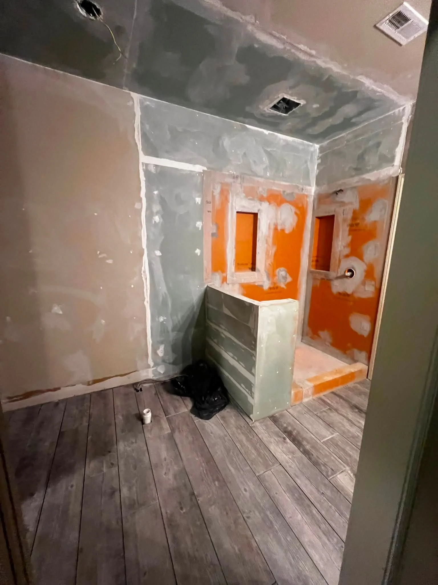 A bathroom under renovation, with drywall and framed spaces for a vanity and mirror. The walls are partially painted with some unfinished areas, and construction materials and tools are on the floor.