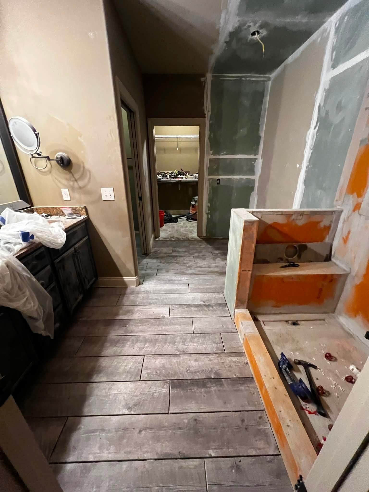 Interior room under renovation with unfinished drywall, a partially built wooden frame, laminate flooring, and construction tools scattered around.