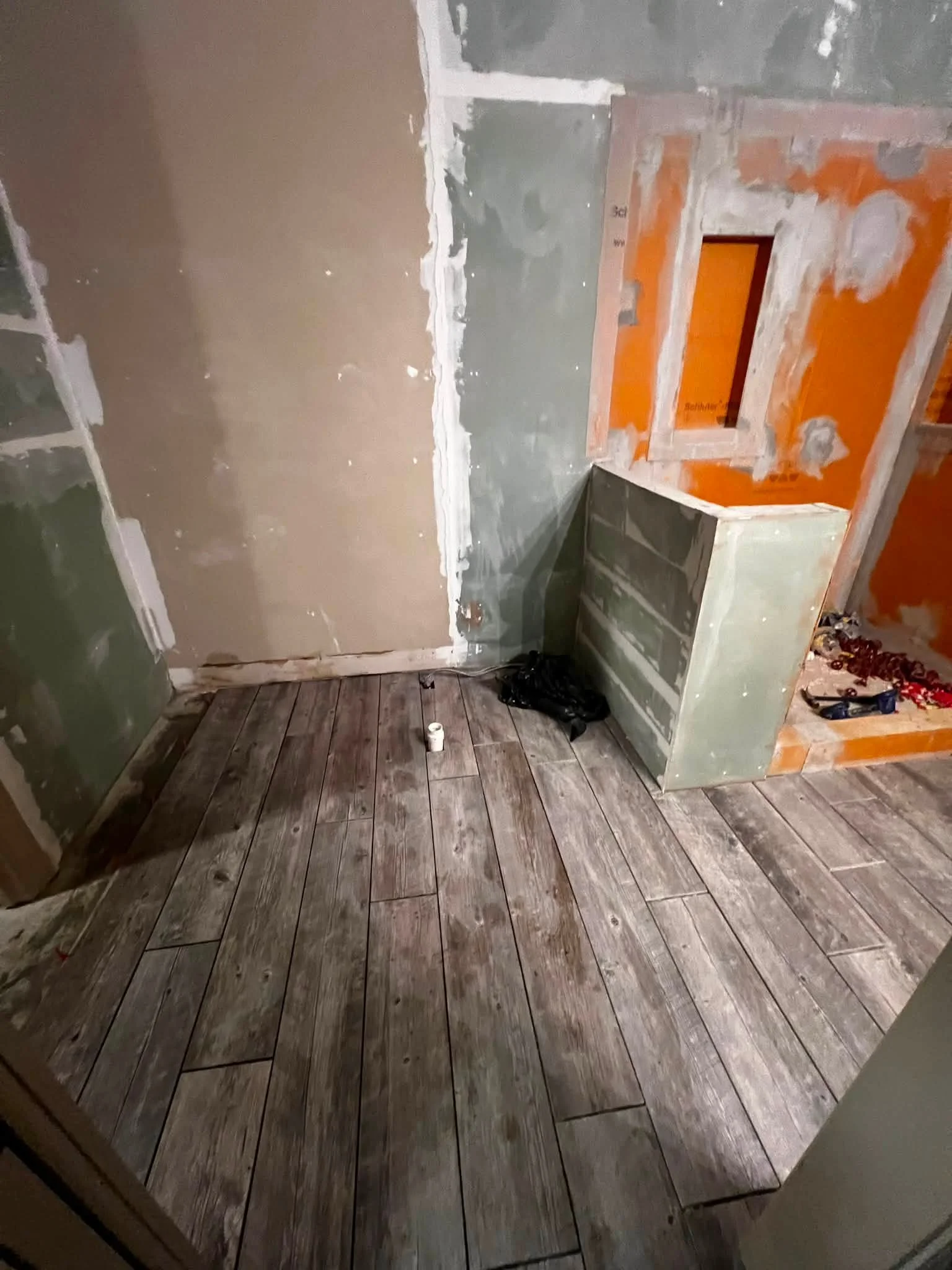 Room under renovation with partially painted walls, unfinished drywall, and a wooden floor with tiles.