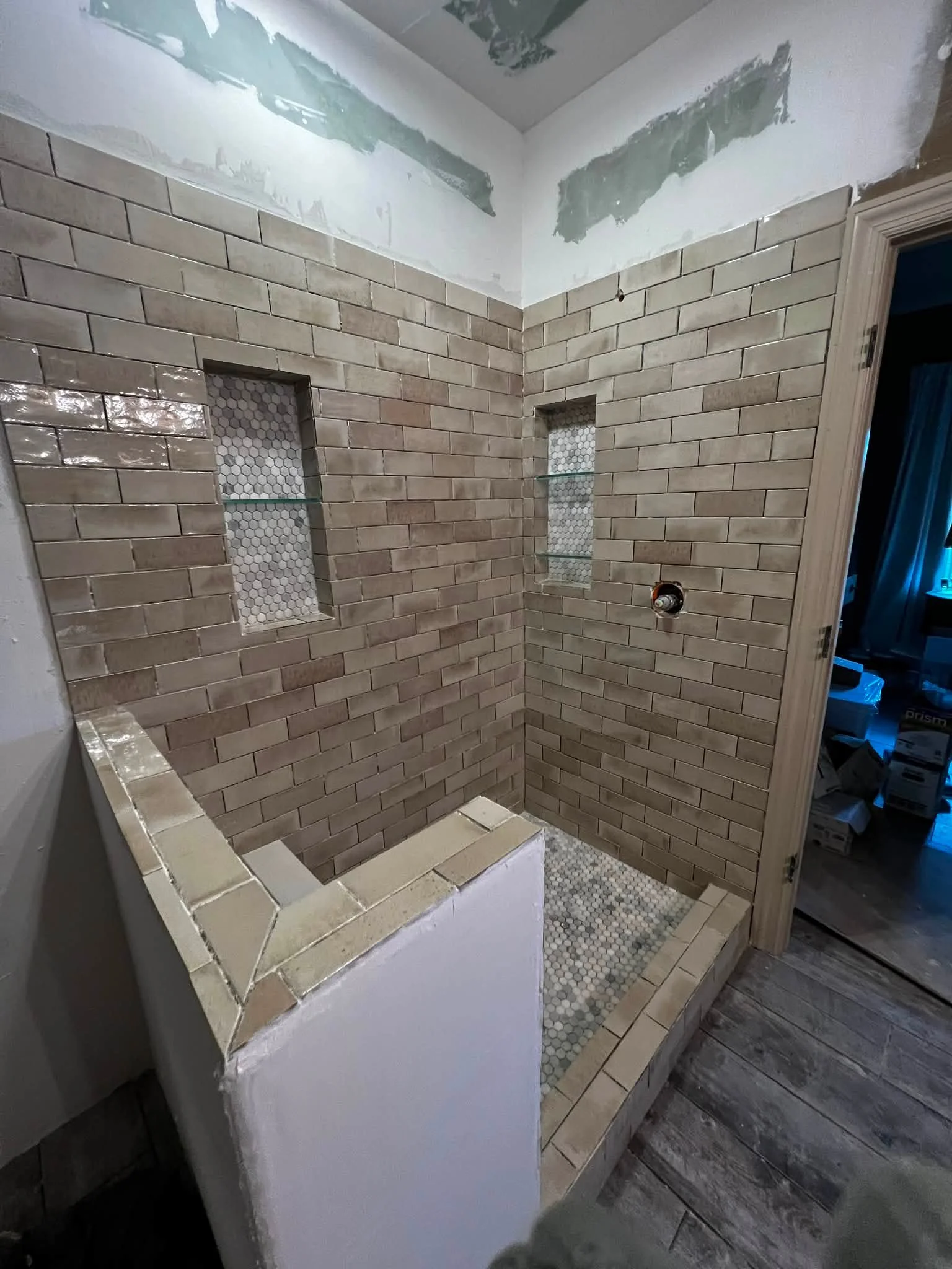 Bathroom under construction with brick wall tiles, two niches with small hexagonal tiles, and a partial shower enclosure.